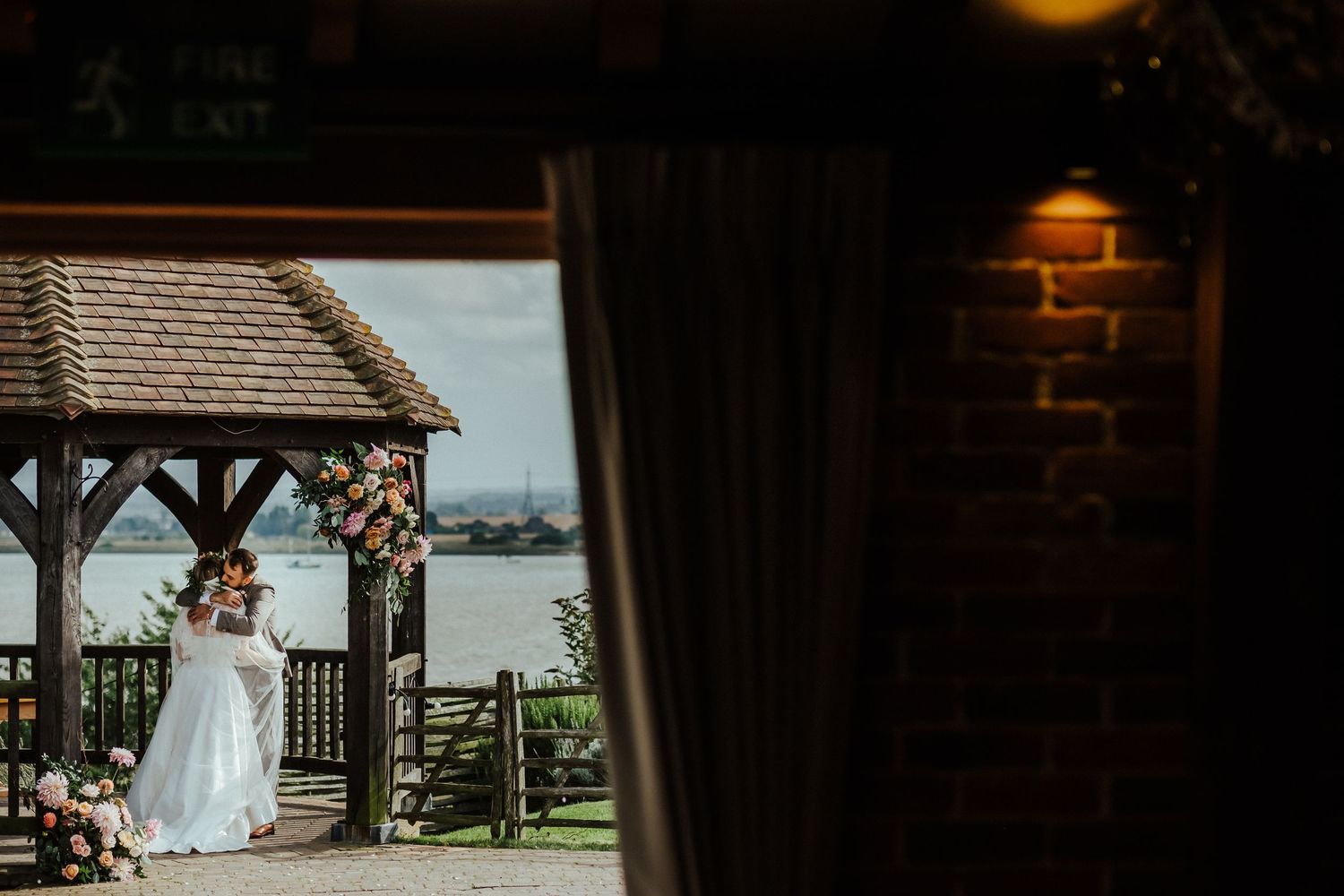 Wedding ceremony setup under wooden gazebo overlooking waterfront view.