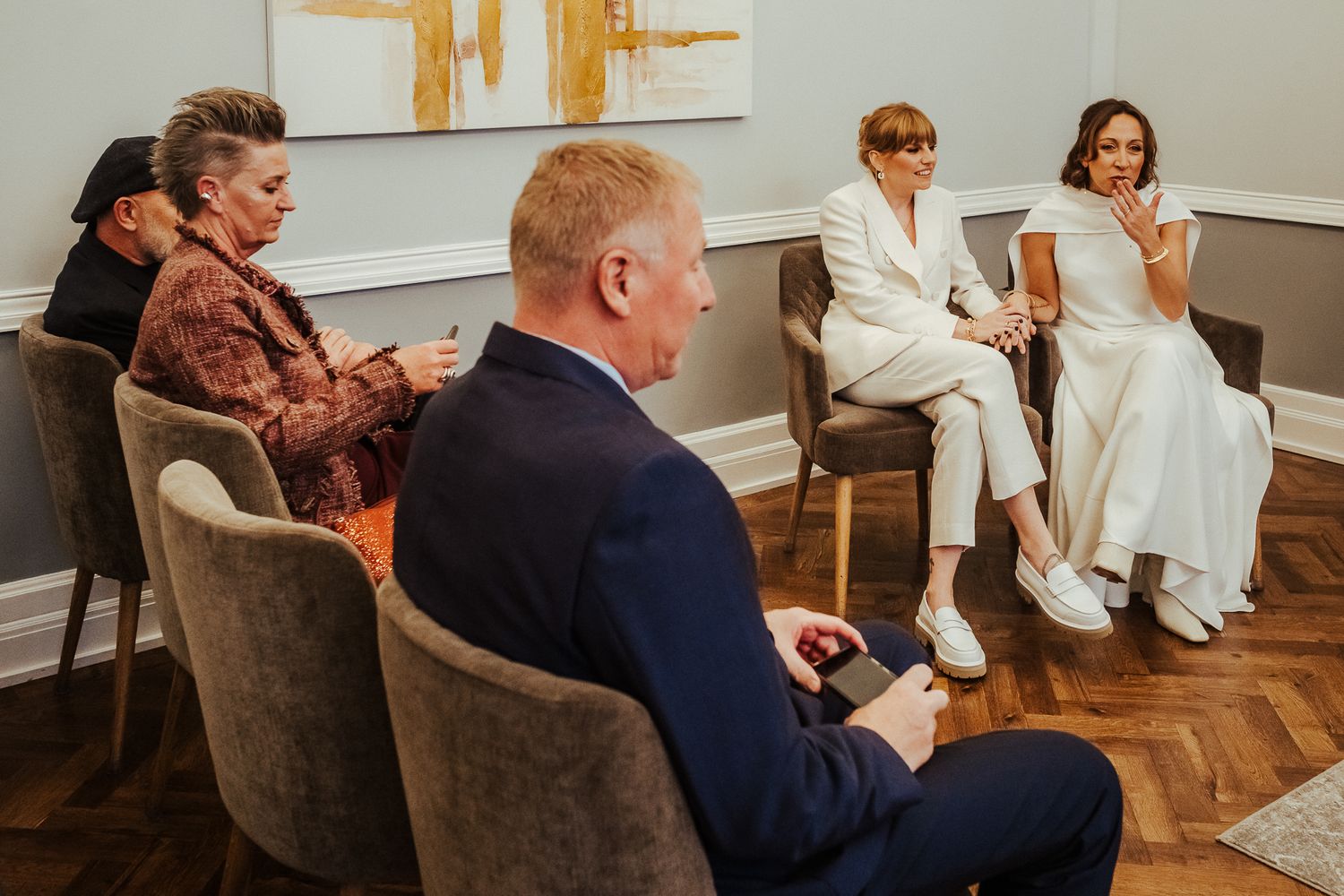 Guests seated in upholstered chairs during an intimate wedding ceremony in a room with wood floors and modern artwork.