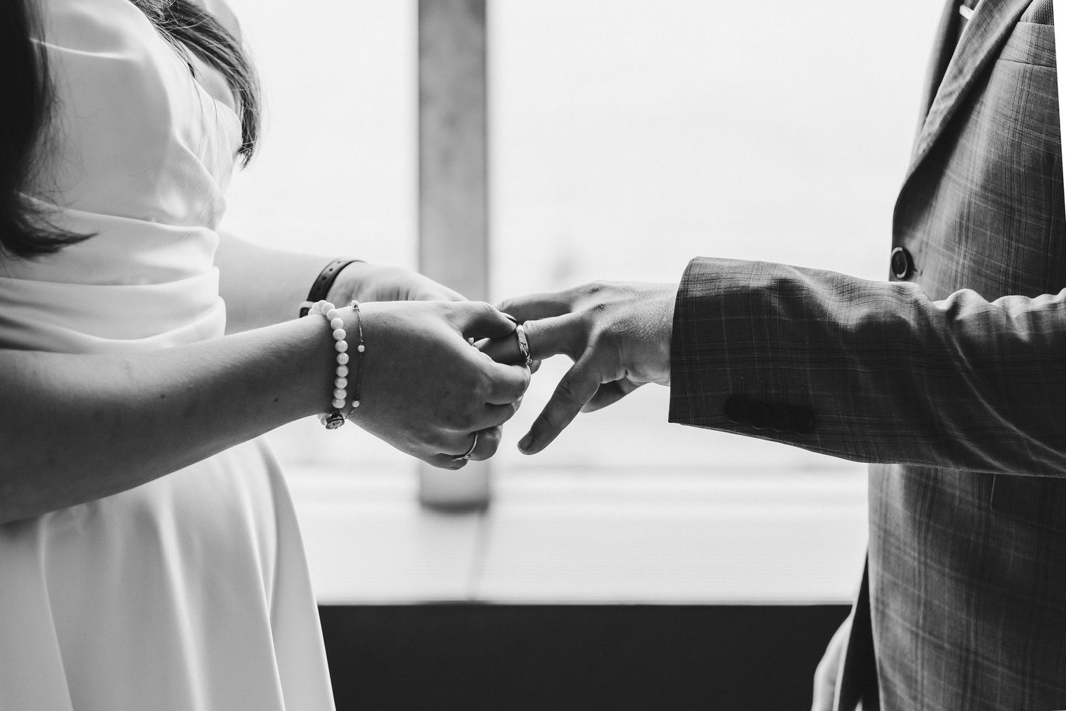 Black and white close-up of couple exchanging rings during wedding ceremony.