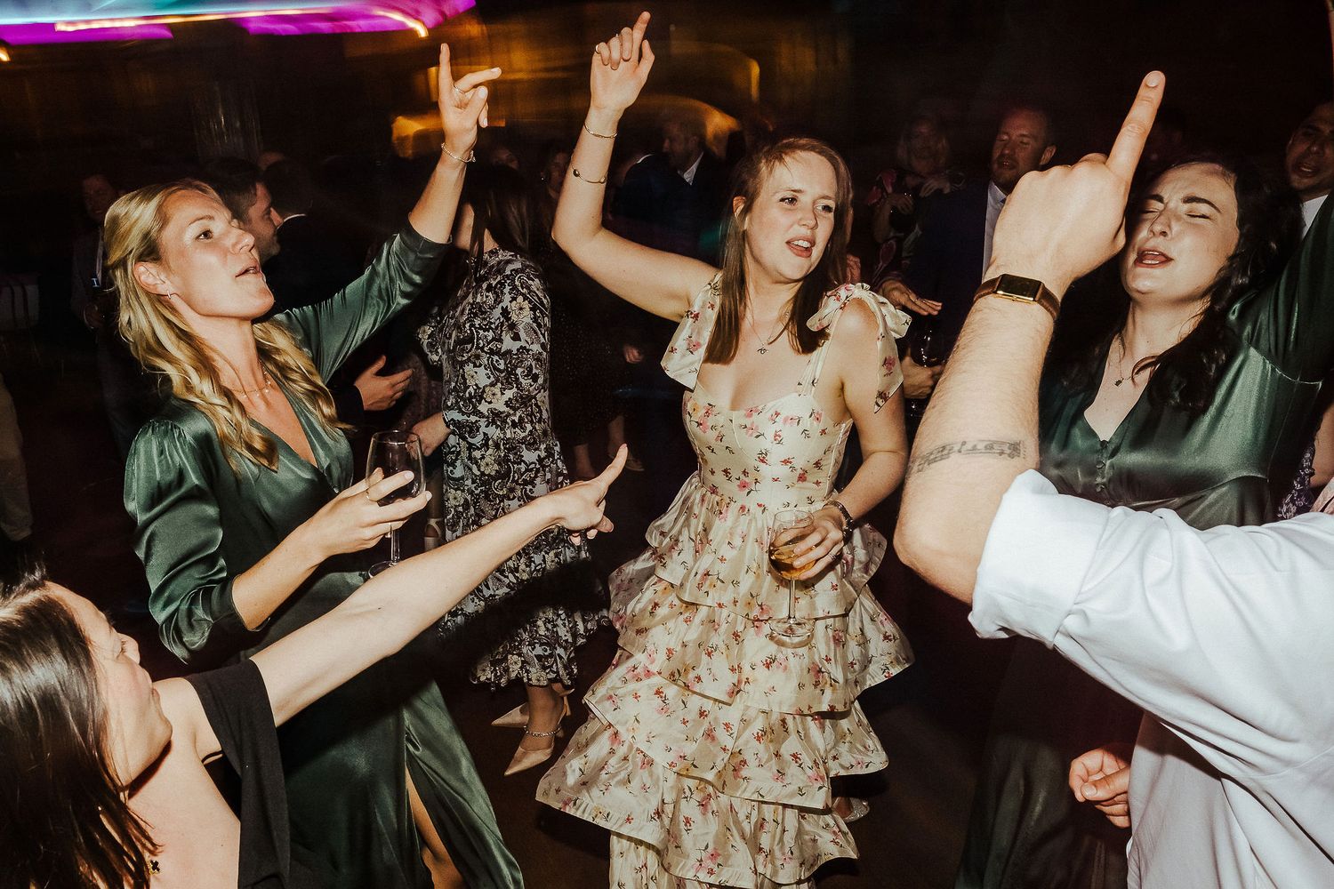 Wedding guests dancing enthusiastically at a reception celebration with colorful lighting.