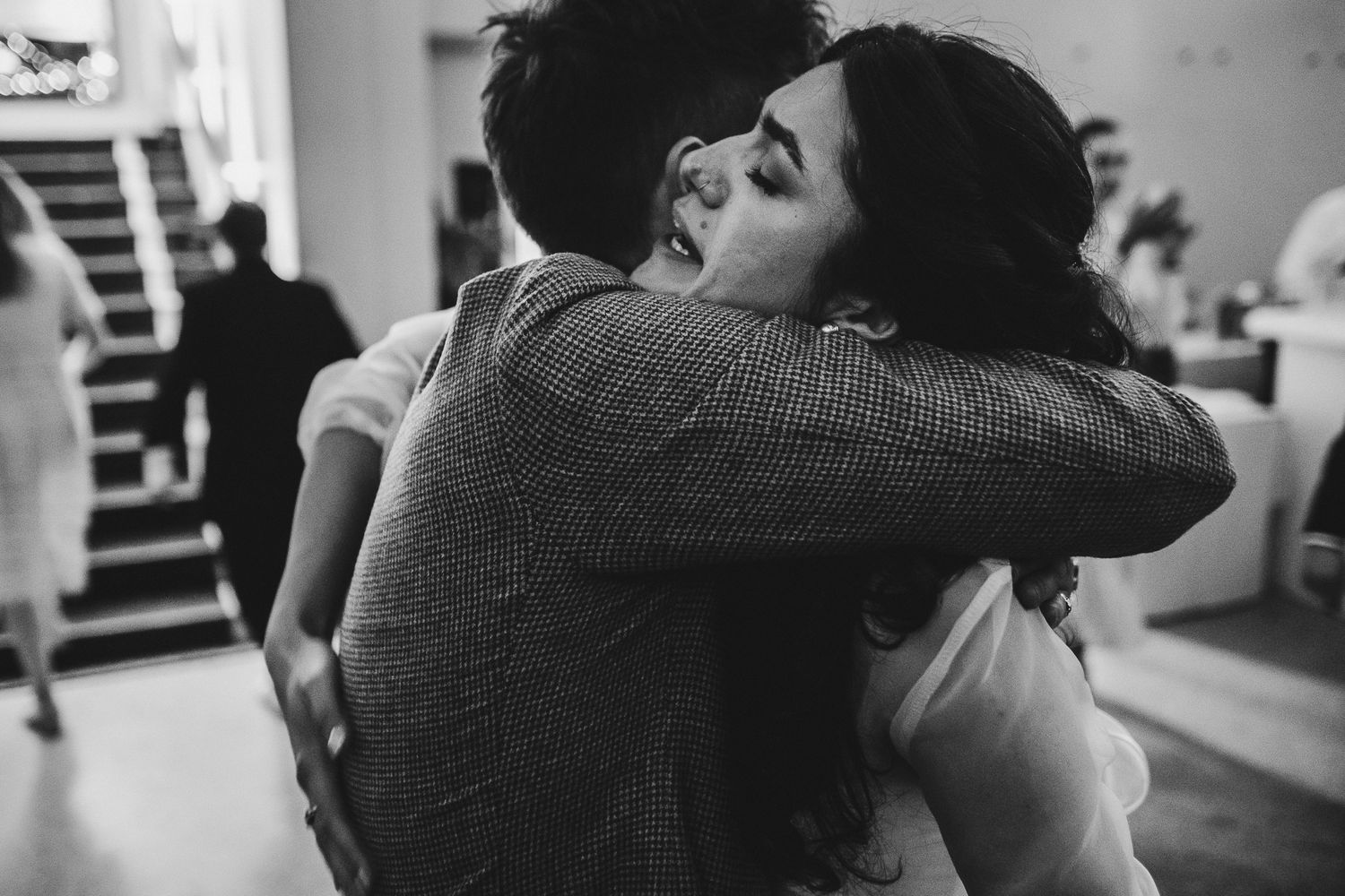 A tender black and white moment captured as two people share an intimate embrace at an indoor event.
