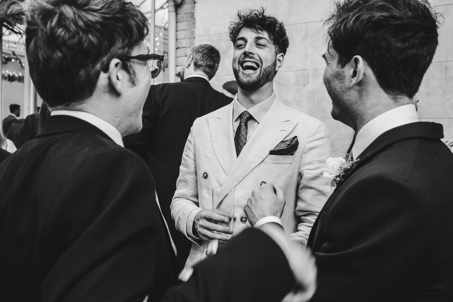 Black and white candid shot of wedding guests sharing laughter and conversation.