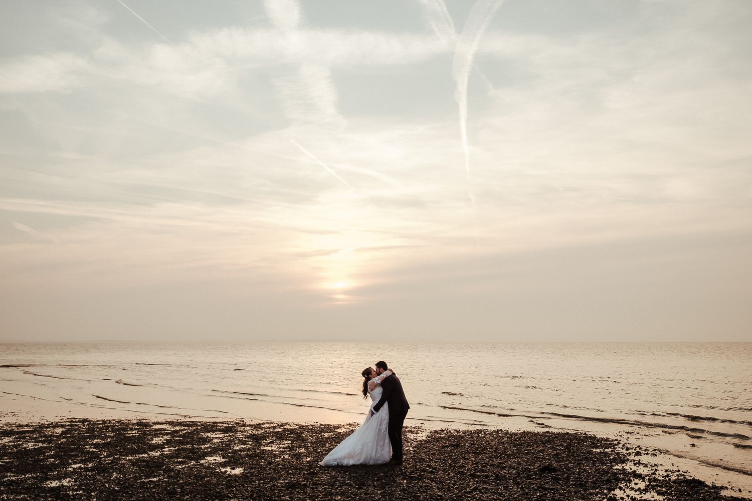 Silhouetted wedding couple stands on beach during golden hour sunset.