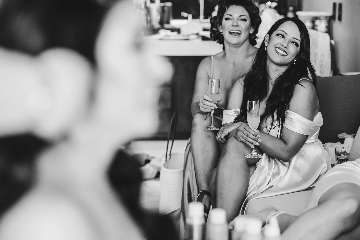 Candid black and white photo of bridal party enjoying drinks during wedding preparations.