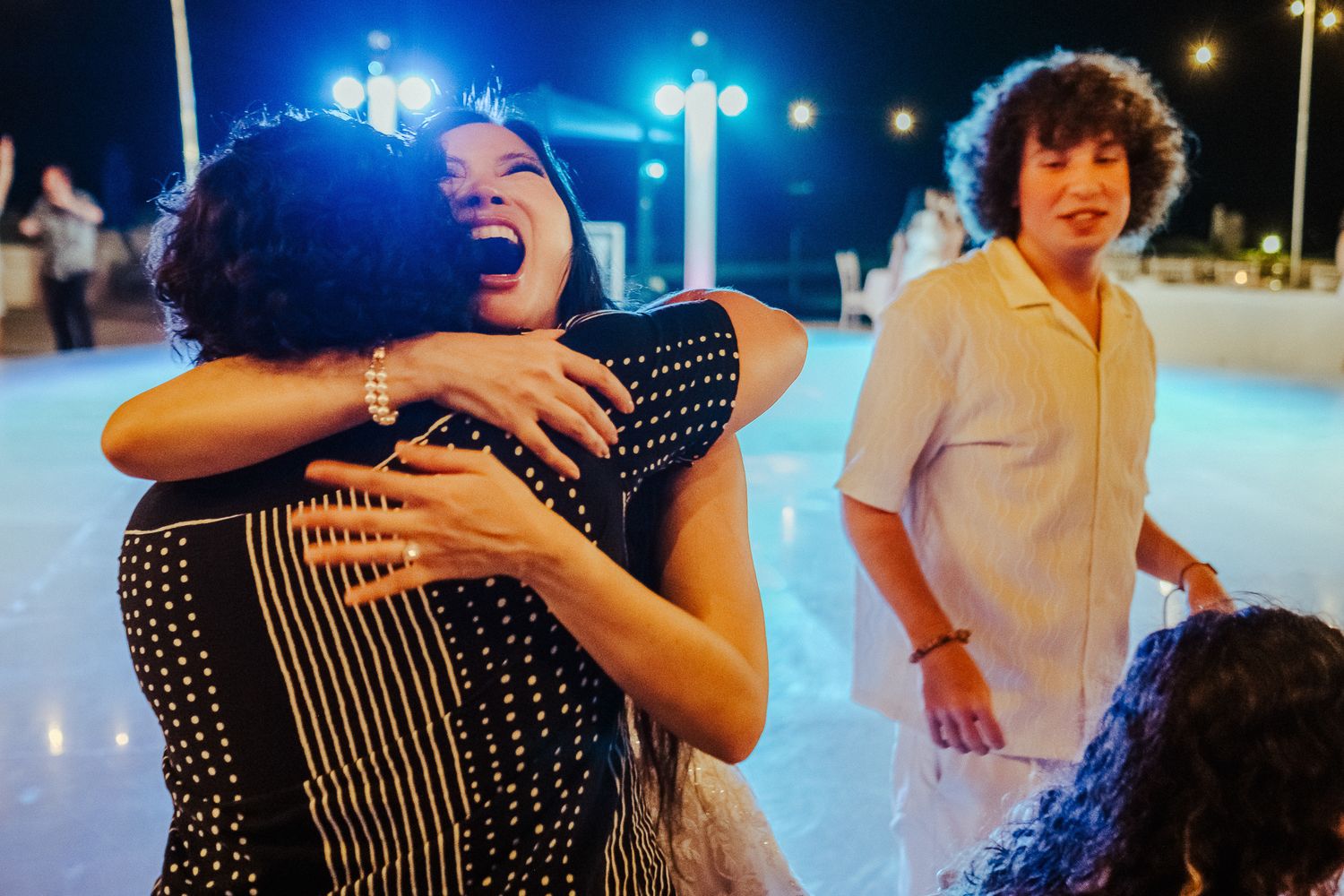 Couples dancing exuberantly under blue lights at an evening celebration.