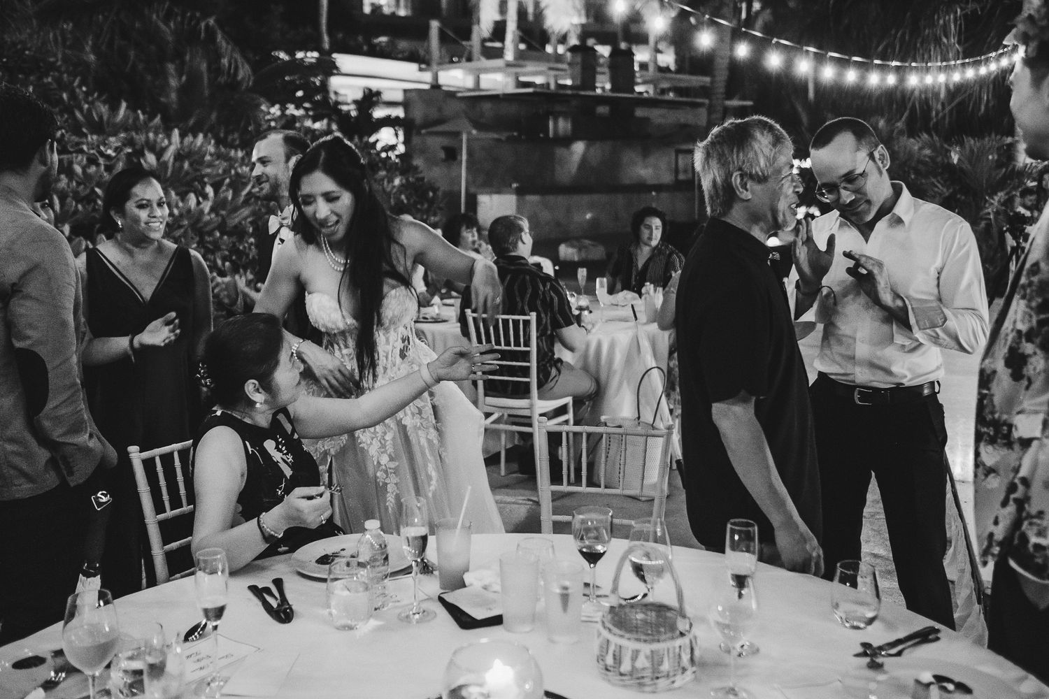 Black and white photo of wedding reception guests mingling around dinner tables.