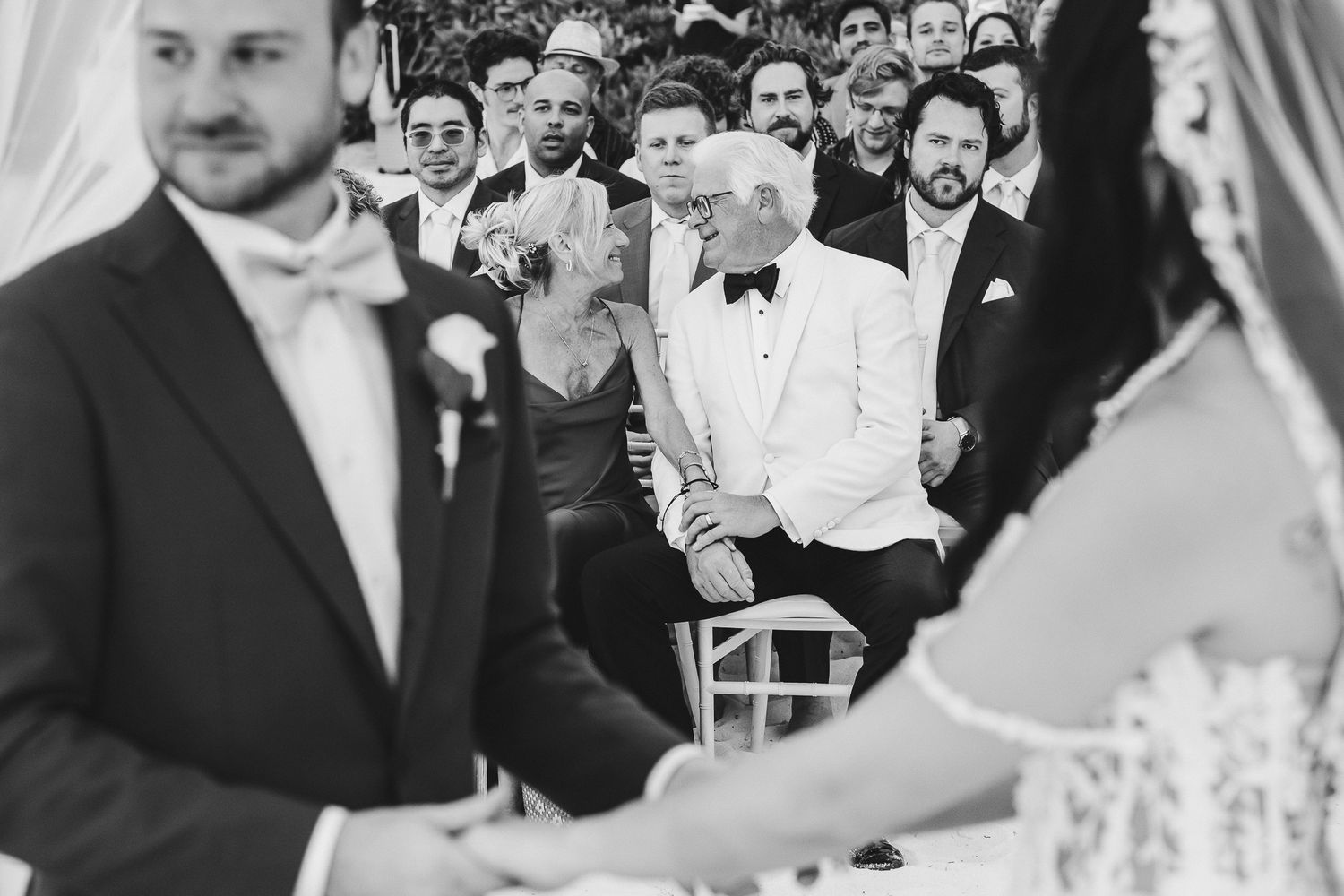 Black and white photo of a wedding ceremony with guests seated and a person in a white suit at the center.