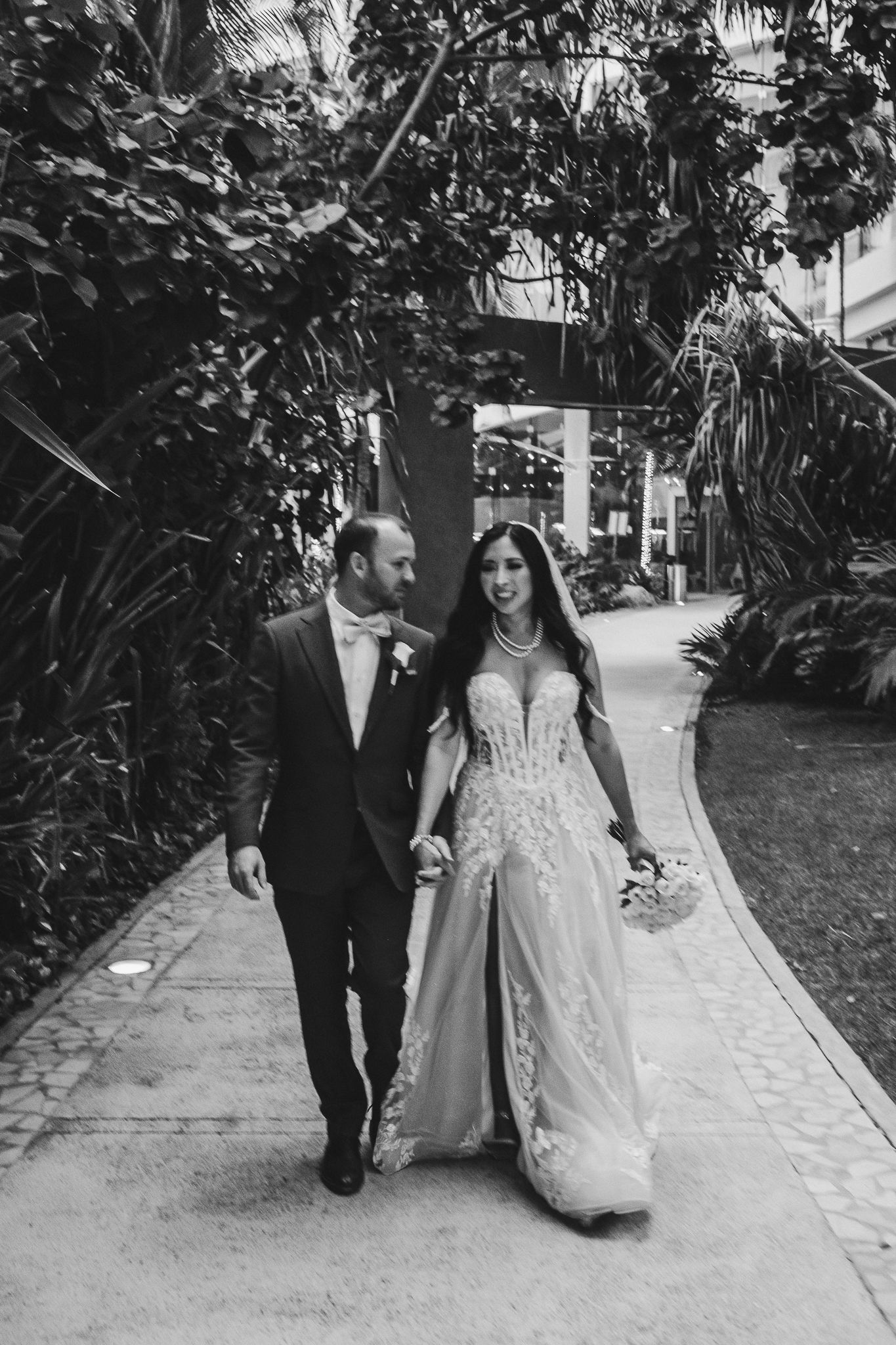 Elegant couple walking down a palm-lined path in black and white on their wedding day.