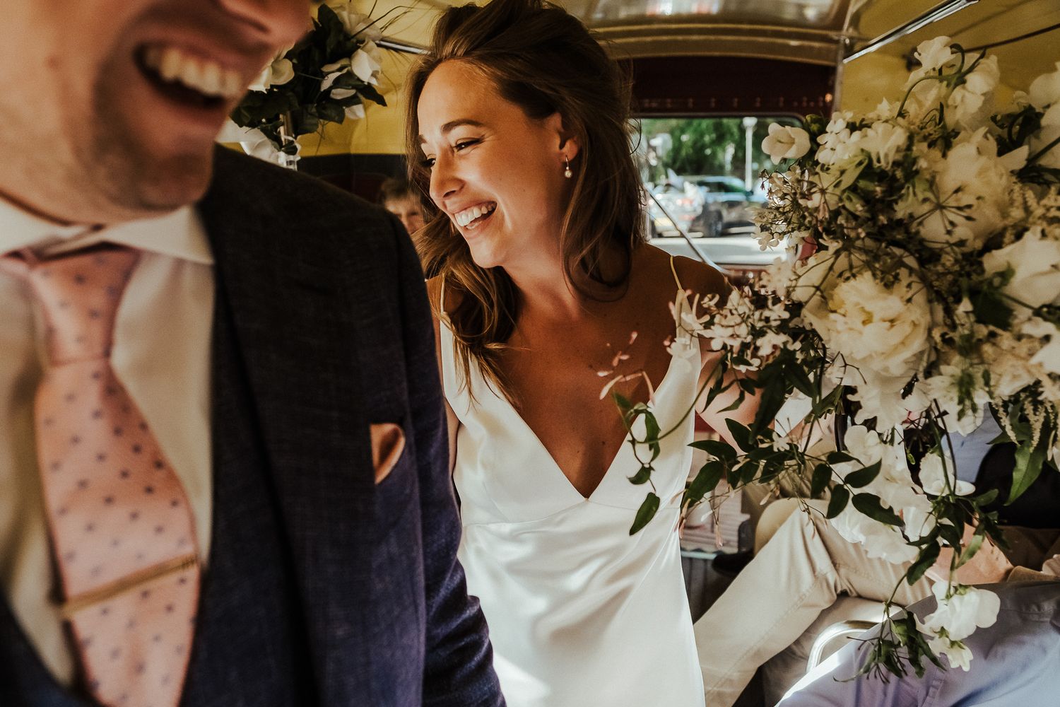 Candid moment of laughter shared in a vintage vehicle decorated with white flowers.