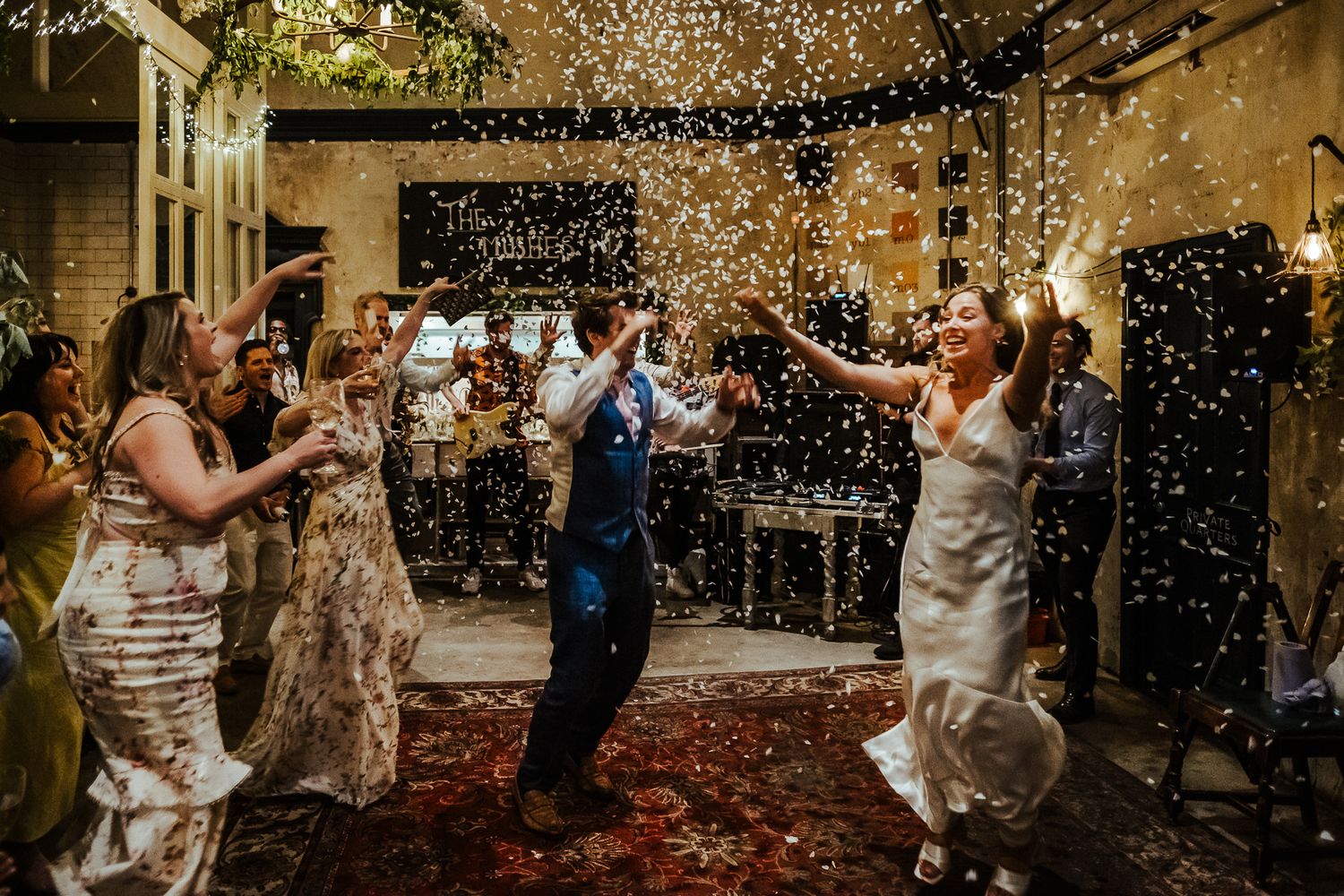 Celebration with confetti raining down on dancing wedding guests in a courtyard.