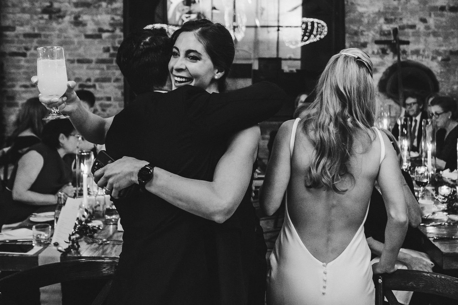 Wedding guests in formal attire celebrate and dance at reception with exposed brick walls.