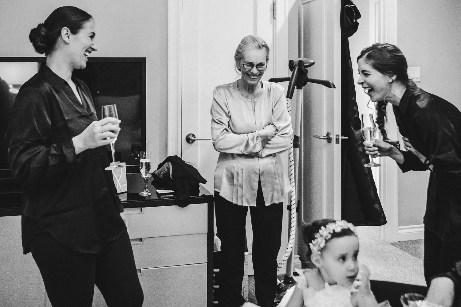 A candid black and white photo of wedding party members sharing drinks and laughter.