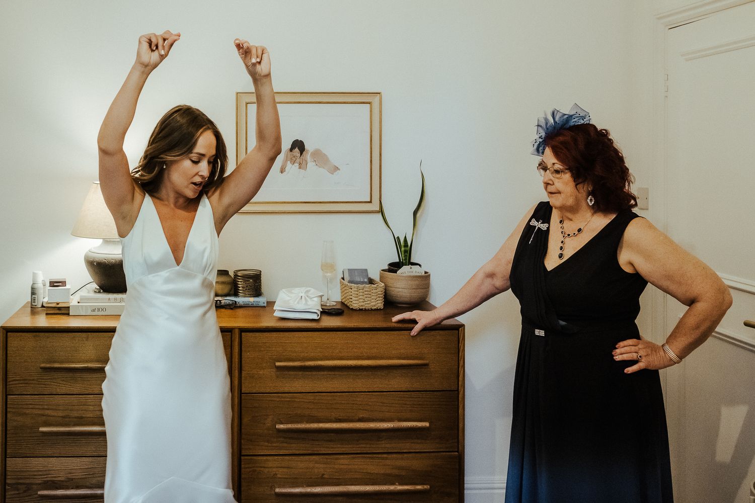 Wedding party members dancing and celebrating with raised arms in a bright indoor space.