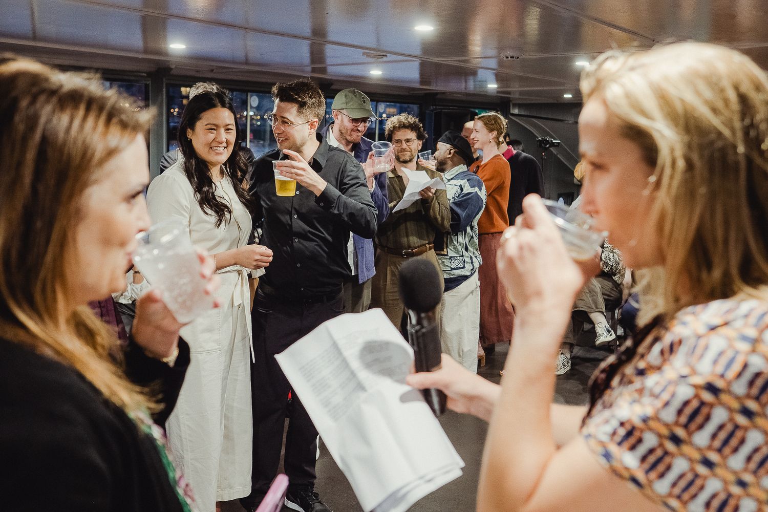 A group of people gathered indoors look at documents and raise glasses in a celebratory toast.