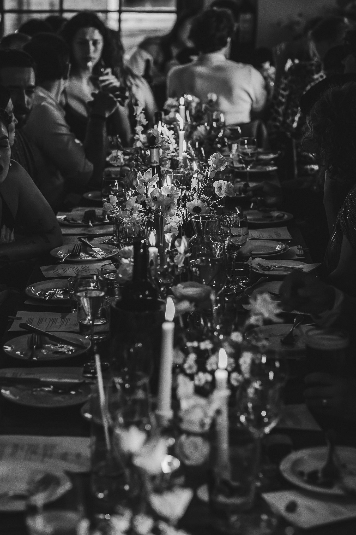Elegant black and white table setting at wedding reception with wine glasses and floral centerpieces down long table.