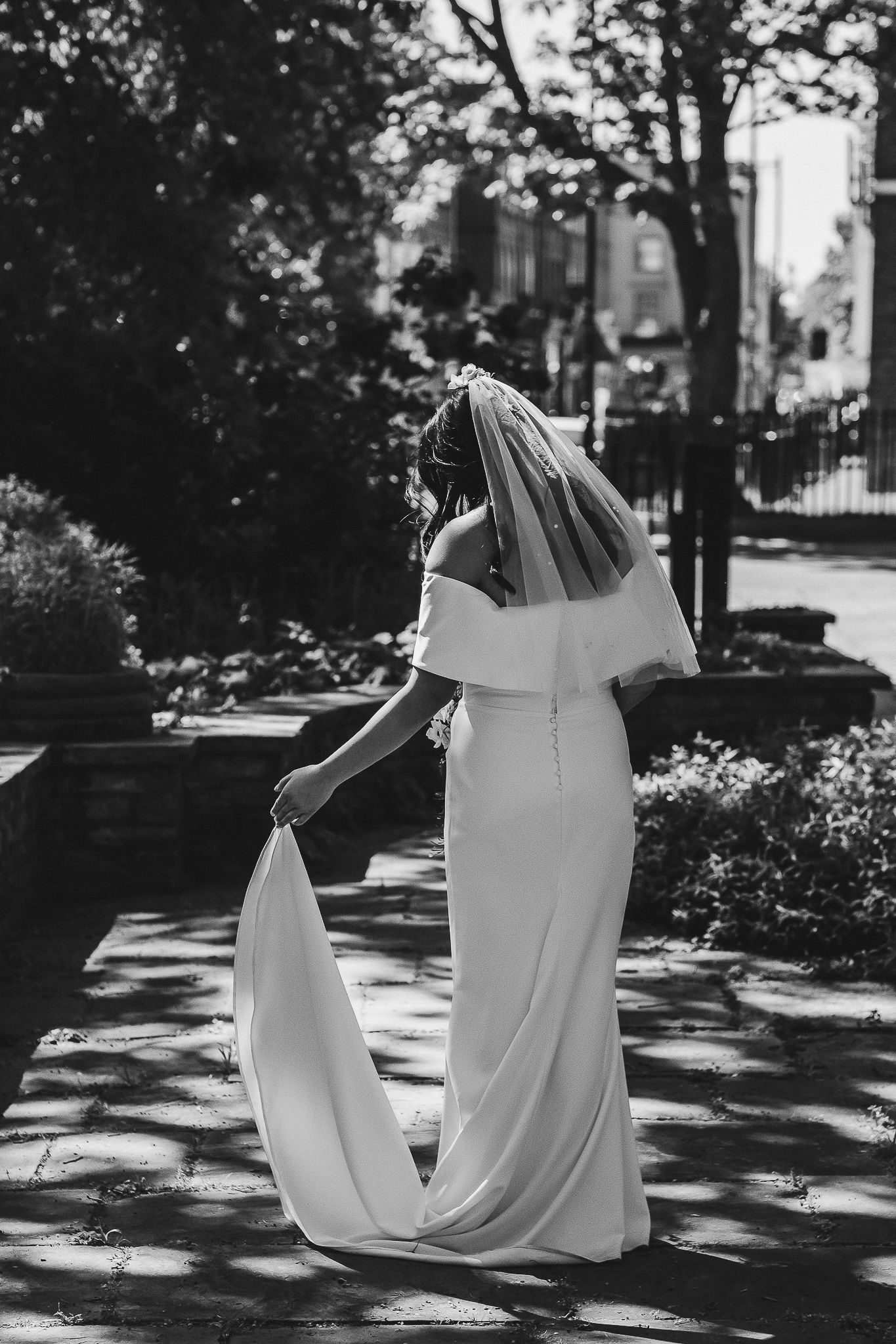 Black and white photo of two people dancing in long white flowing dresses creating elegant shadows on a garden path.
