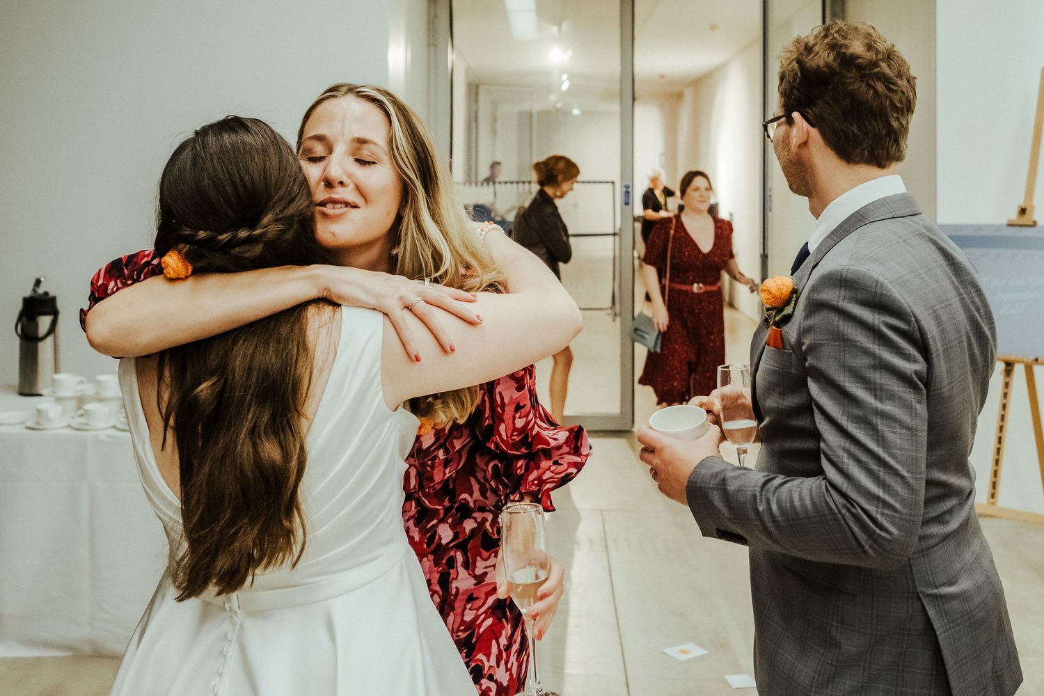 Wedding guests share an emotional embrace while celebrating at an indoor reception venue.