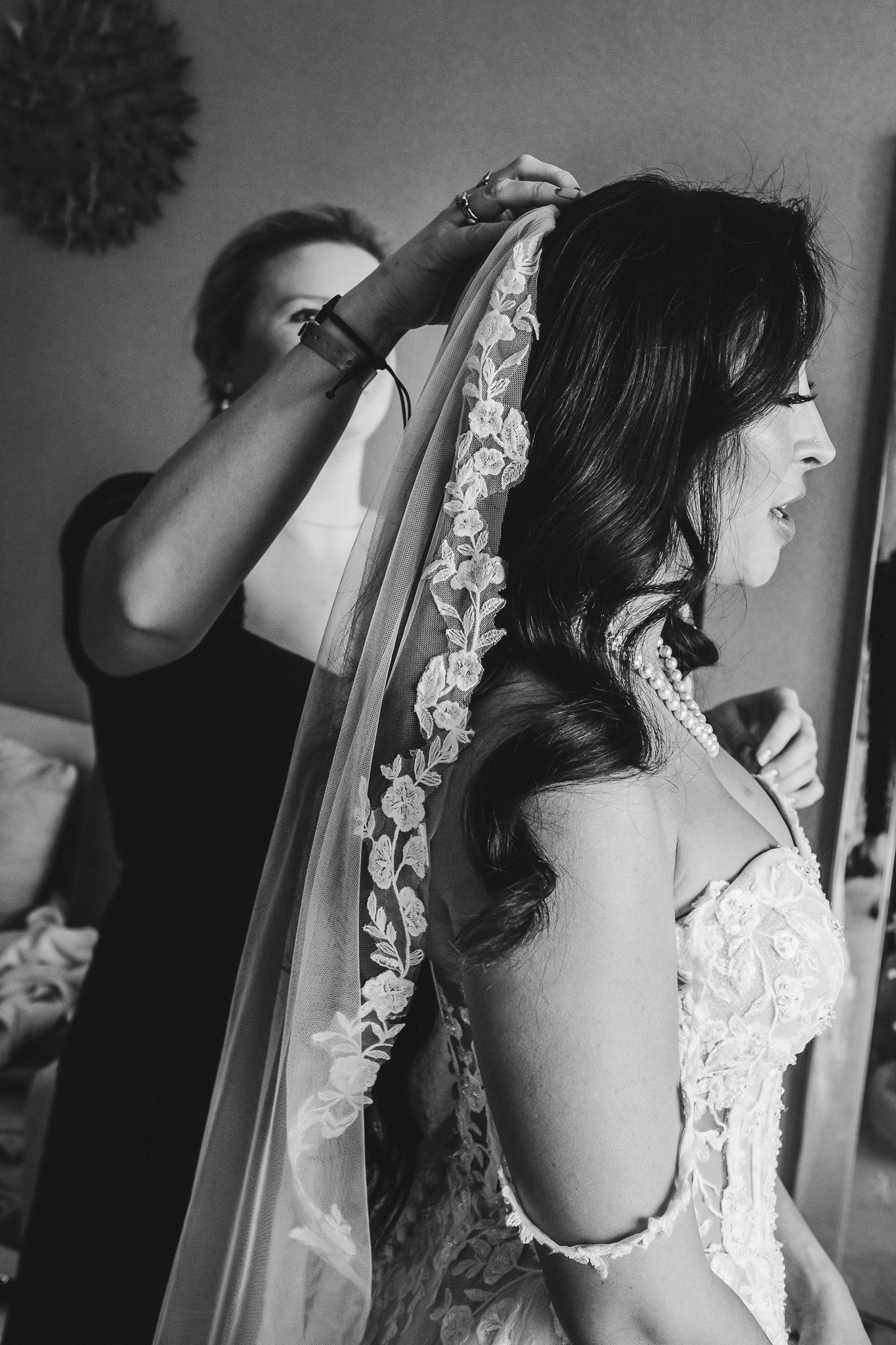 Black and white photo of veil being attached during bridal preparation.