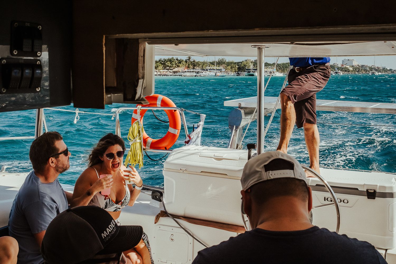 People enjoying drinks and conversation on a boat deck with blue ocean waters in the background.