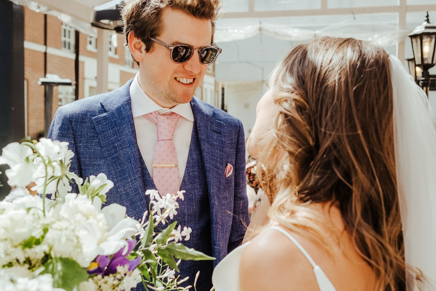 An intimate wedding moment captured with sunlit floral arrangements and vintage architecture.