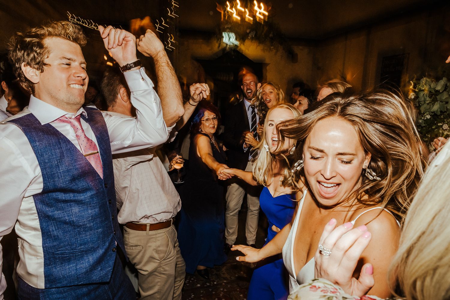 Wedding guests dancing and celebrating with joyful expressions under warm lighting.