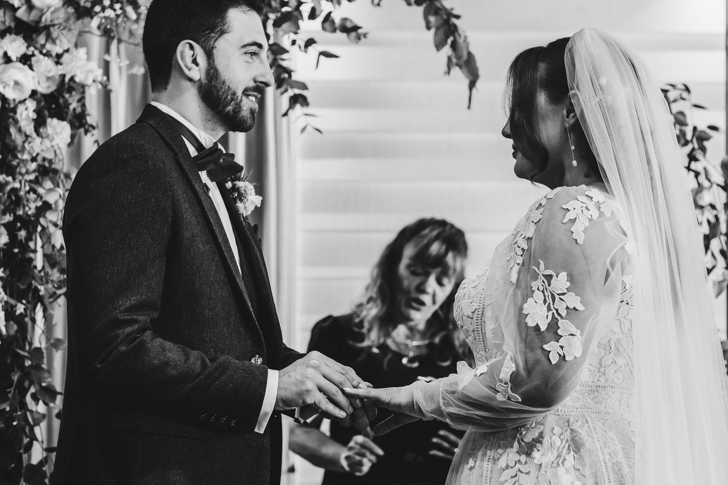 Black and white photo of wedding ceremony with couple exchanging rings.