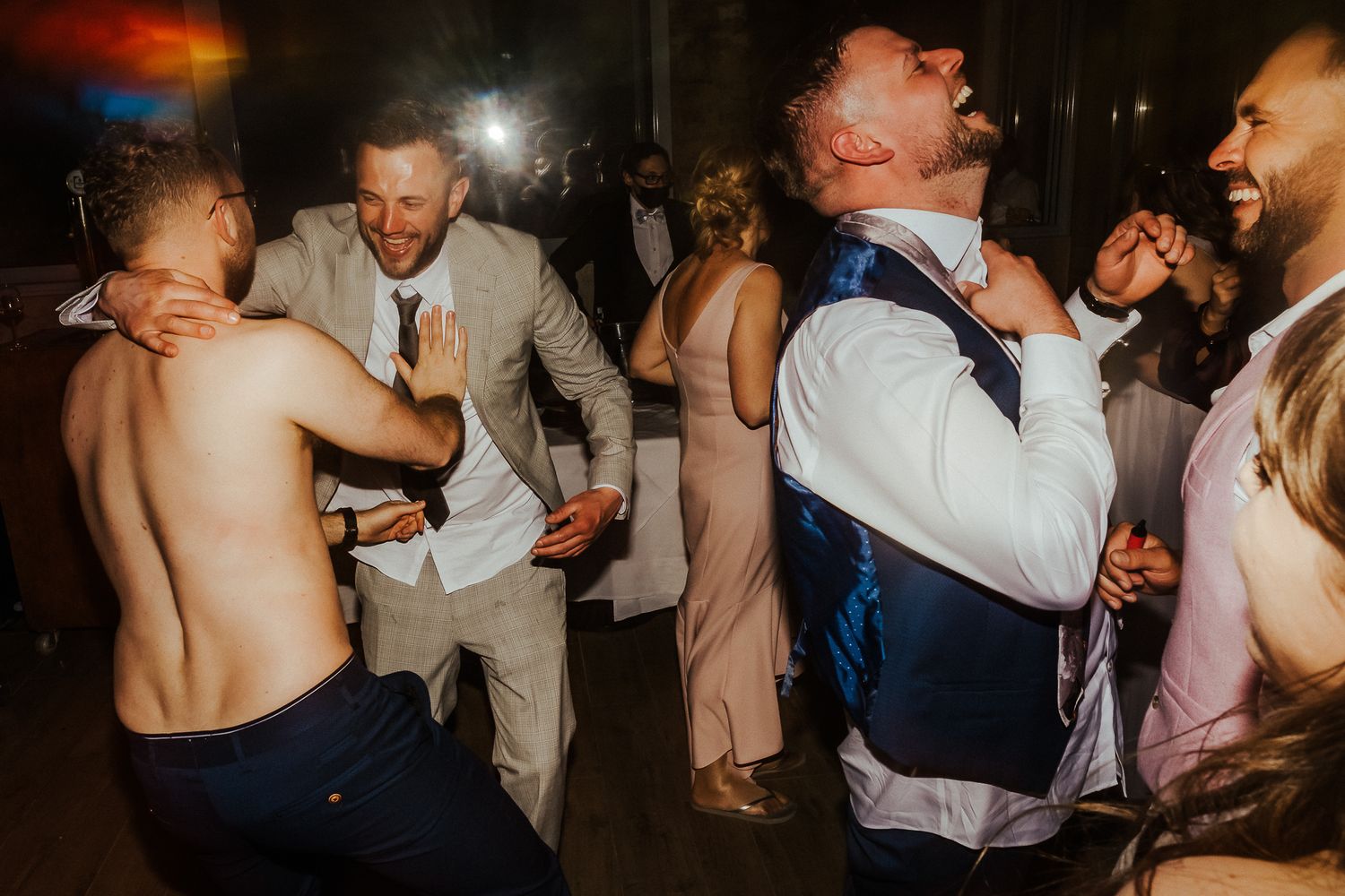 Energetic wedding guests dancing and celebrating at a dimly lit reception party.