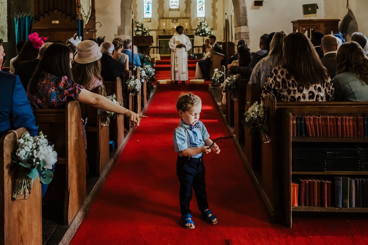 A young ring bearer in blue stands in the center aisle of a church during a wedding ceremony.