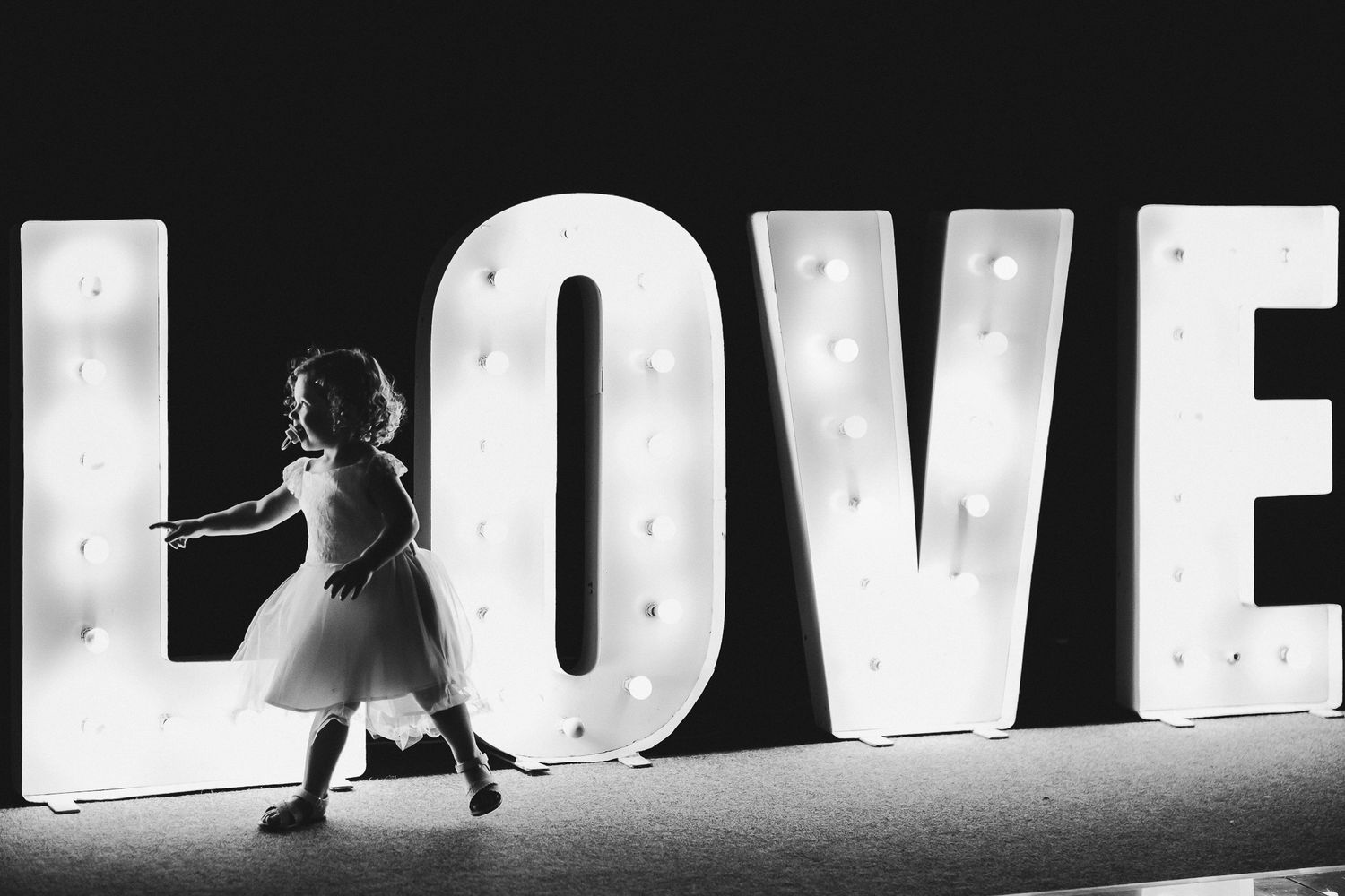 Small silhouette against large illuminated LOVE letters at wedding venue.