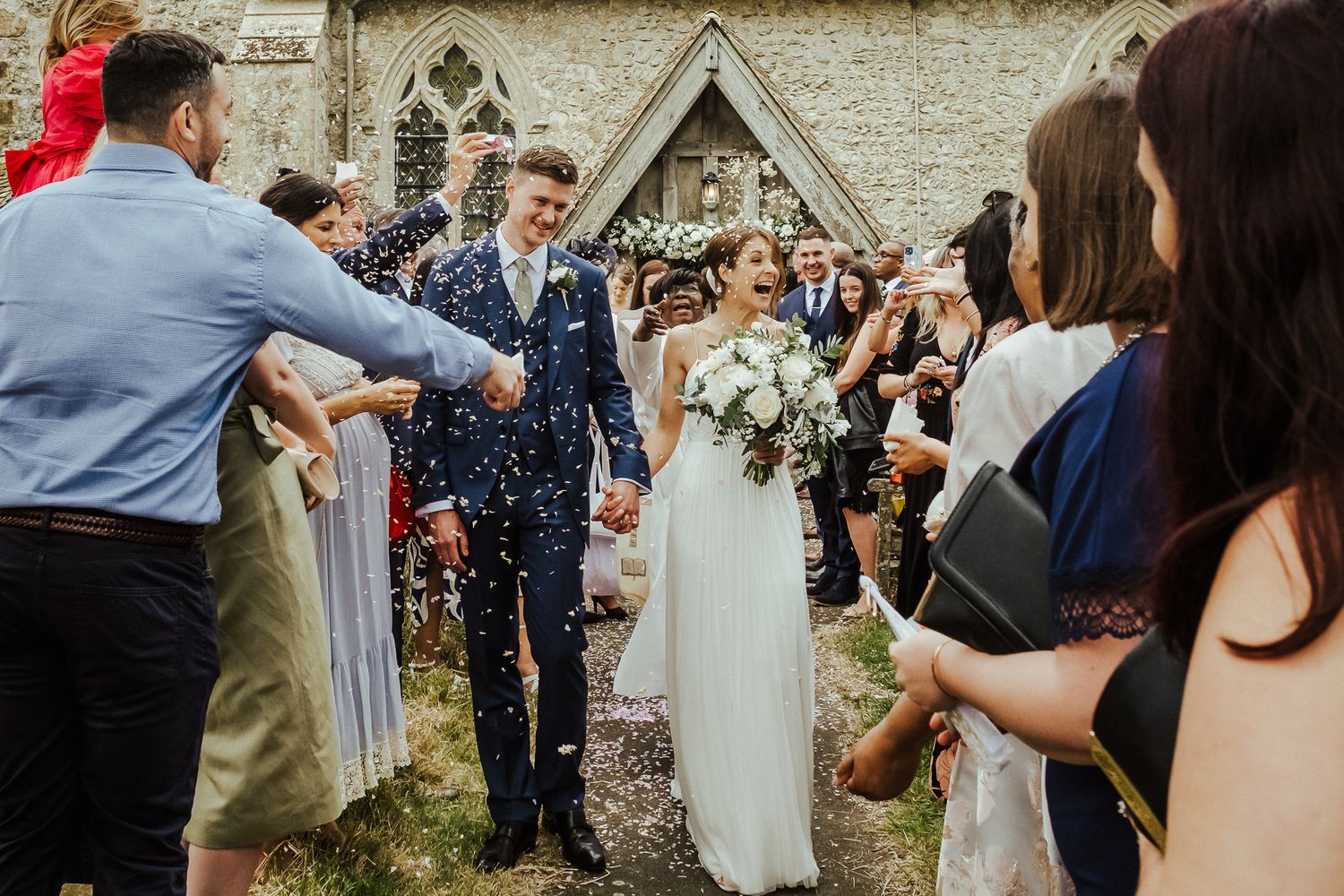 Wedding guests celebrating with confetti outside a stone church building.