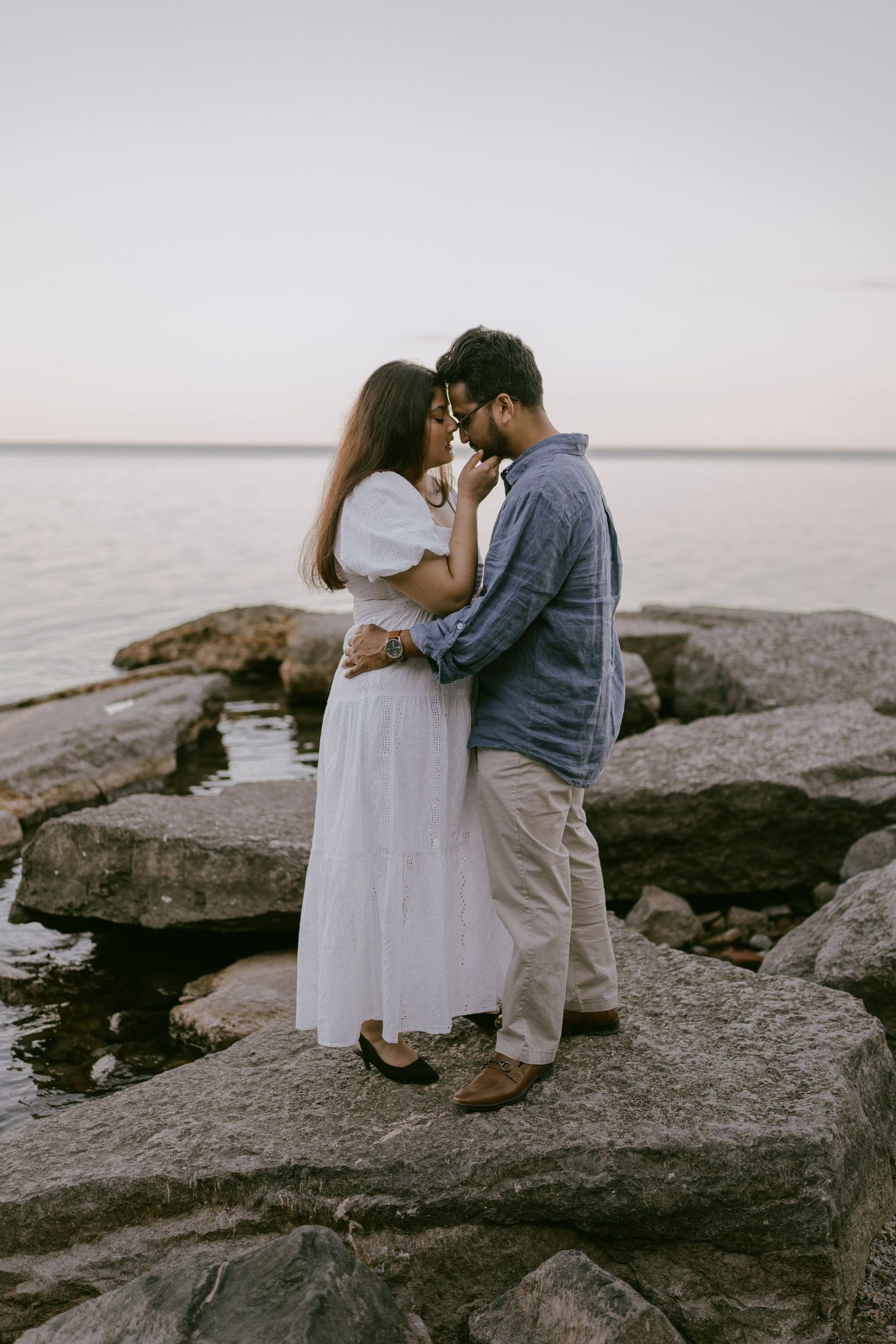 Couple embracing on rocky lakeshore at sunset in Oshawa, Ontario, available throughout Toronto and Durham region