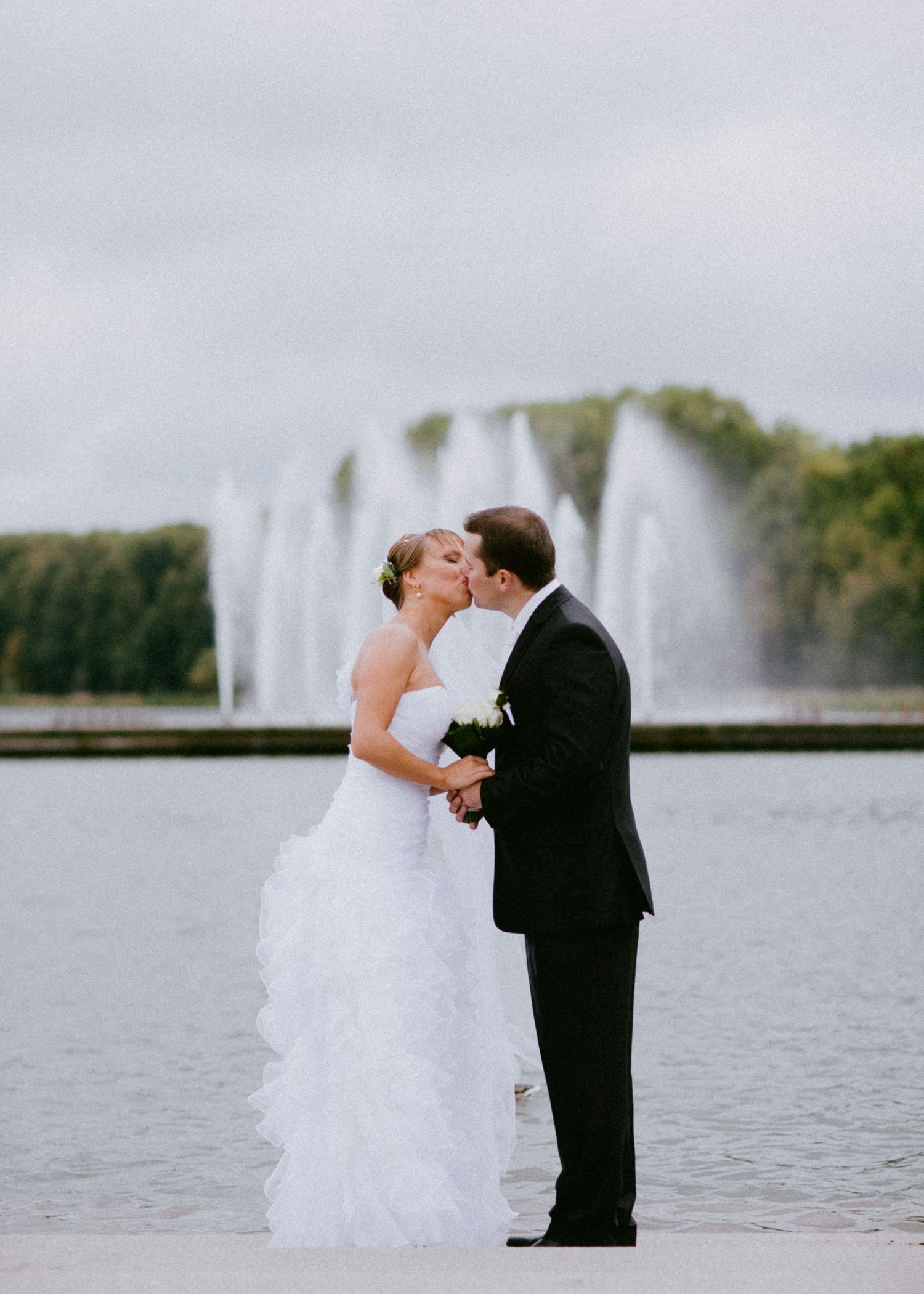 Bride and groom kissing in front of water fountain during portraits in Oshawa, Ontario, available throughout Toronto and Durham region