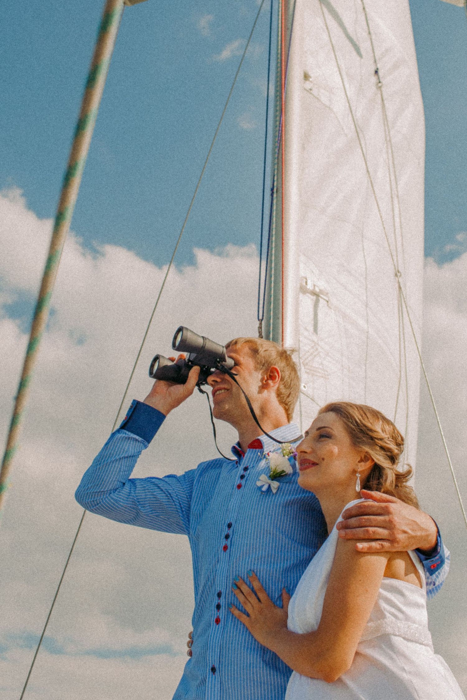 Playful wedding photo of couple sailing and using binoculars under a clear blue sky in Oshawa, available throughout Toronto and Durham regi