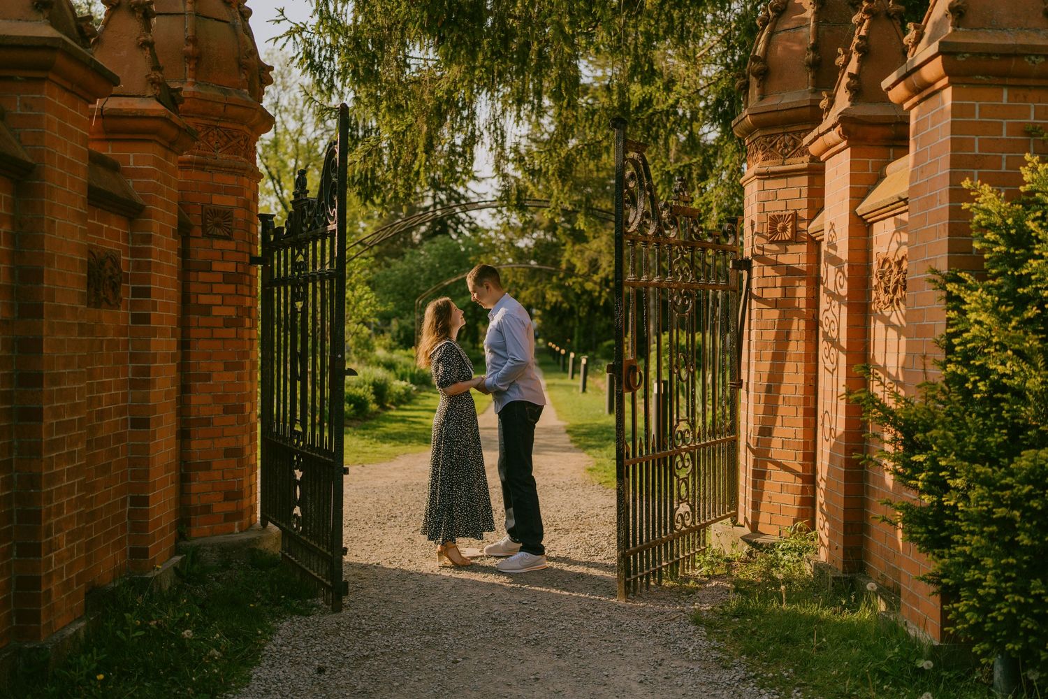 Golden hour engagement photo of couple walking through red brick garden gate in Toronto