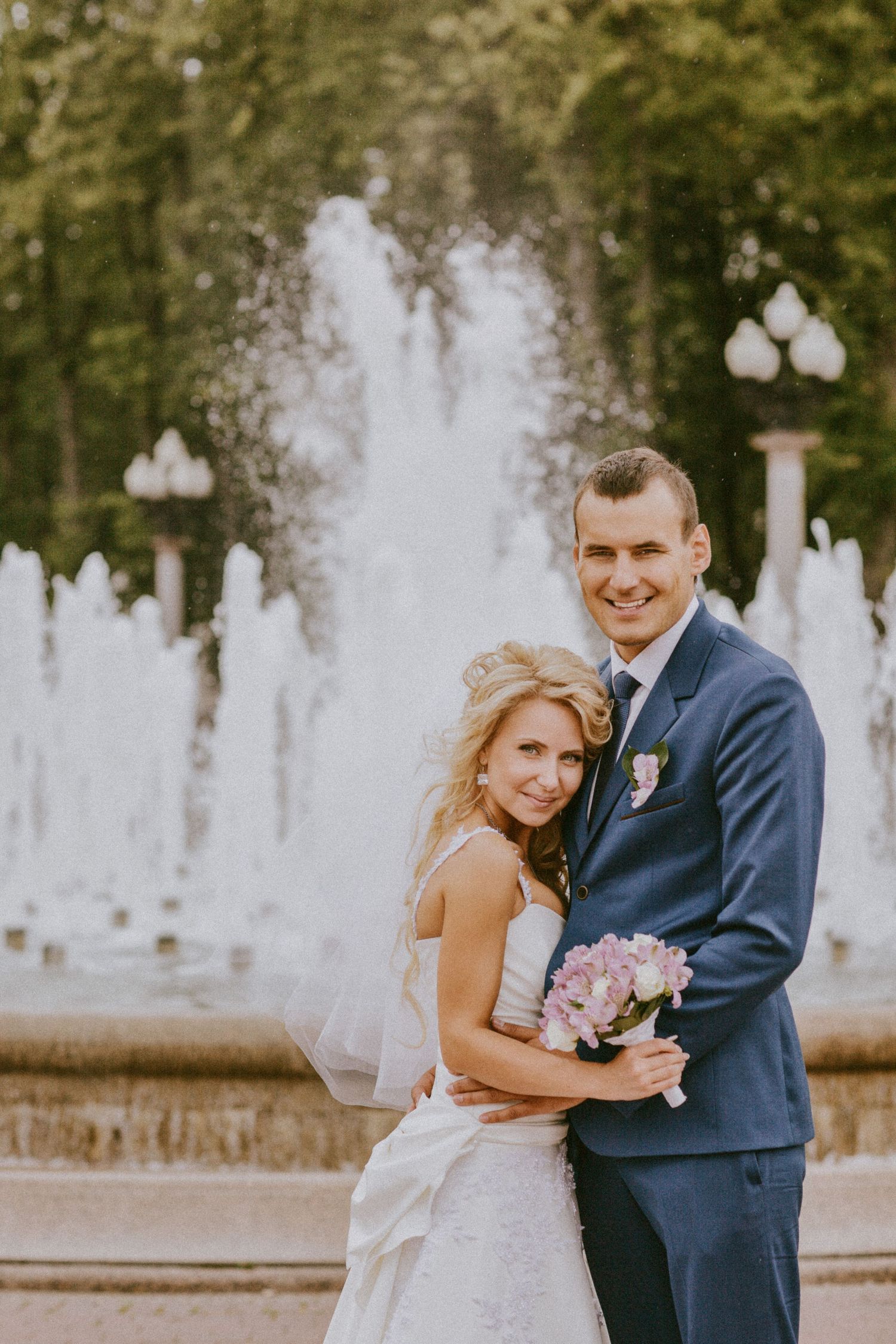 Bride and groom smiling in front of a city fountain, holding bouquet in Oshawa, Ontario, available throughout Toronto and Durham region