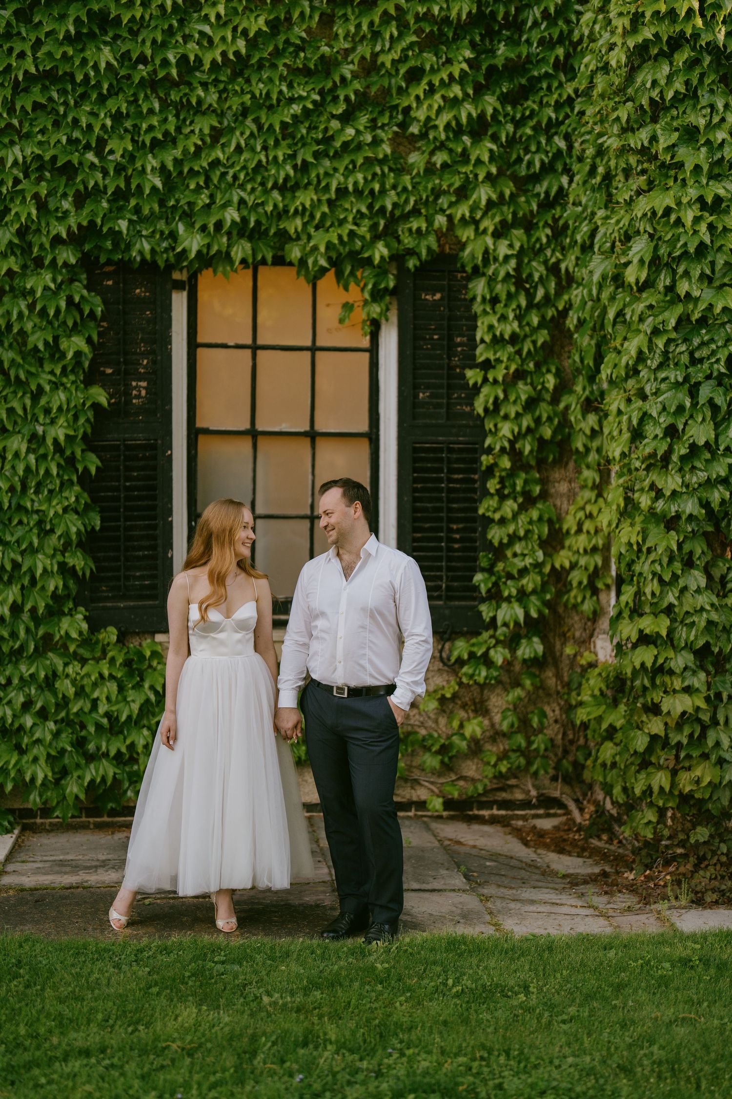 Elegant couple portrait in front of ivy-covered building and black window in Toronto
