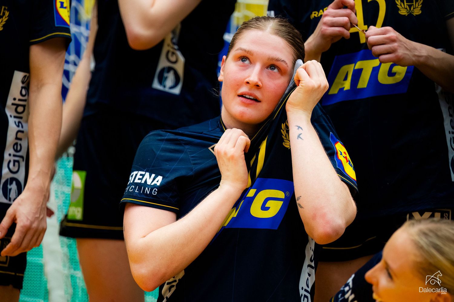 Enthusiastic cheerleader in black jersey and yellow uniform performs energetic dance routine during indoor sporting event.