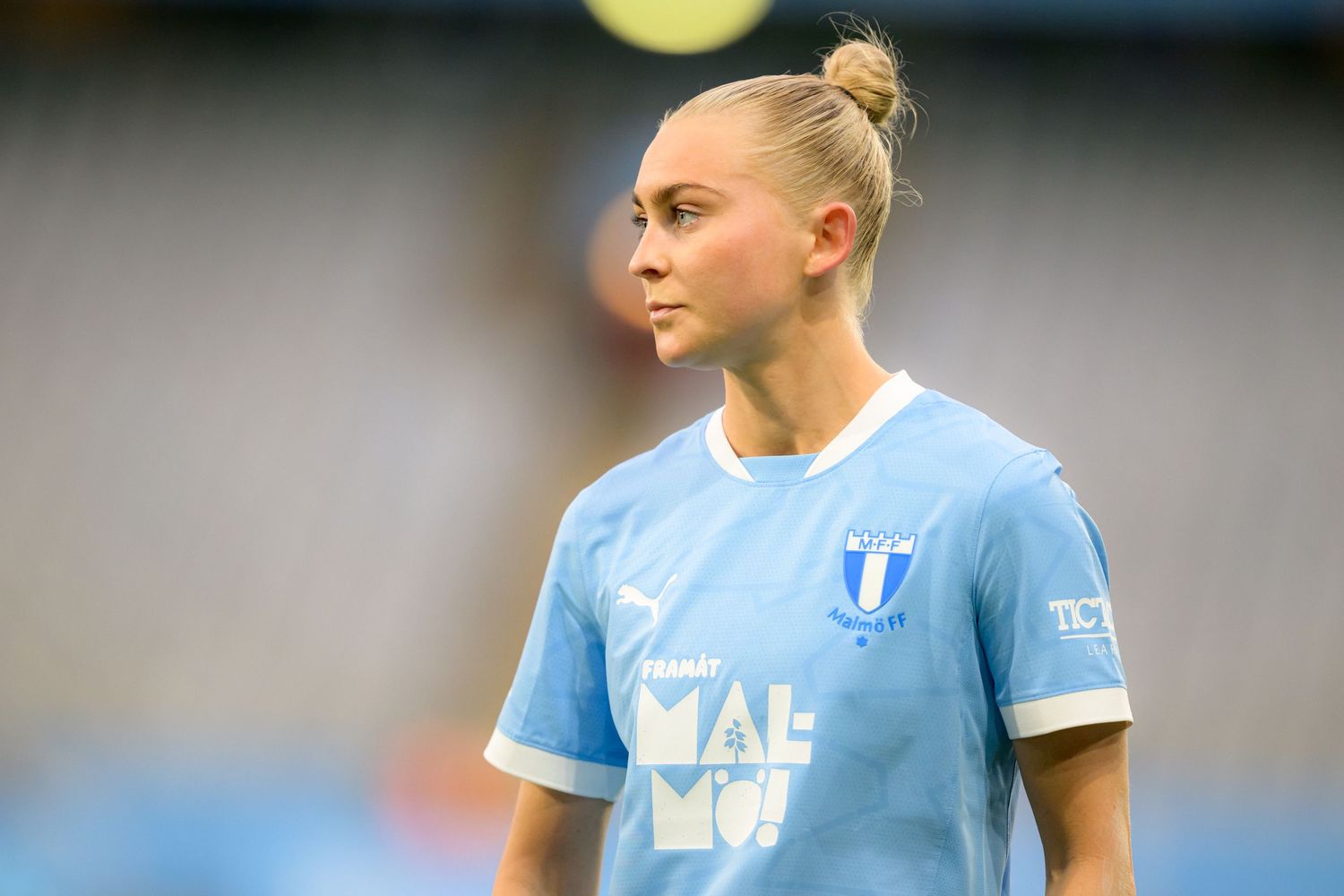 Soccer player wearing a light blue jersey with white trim stands on the field during a match.