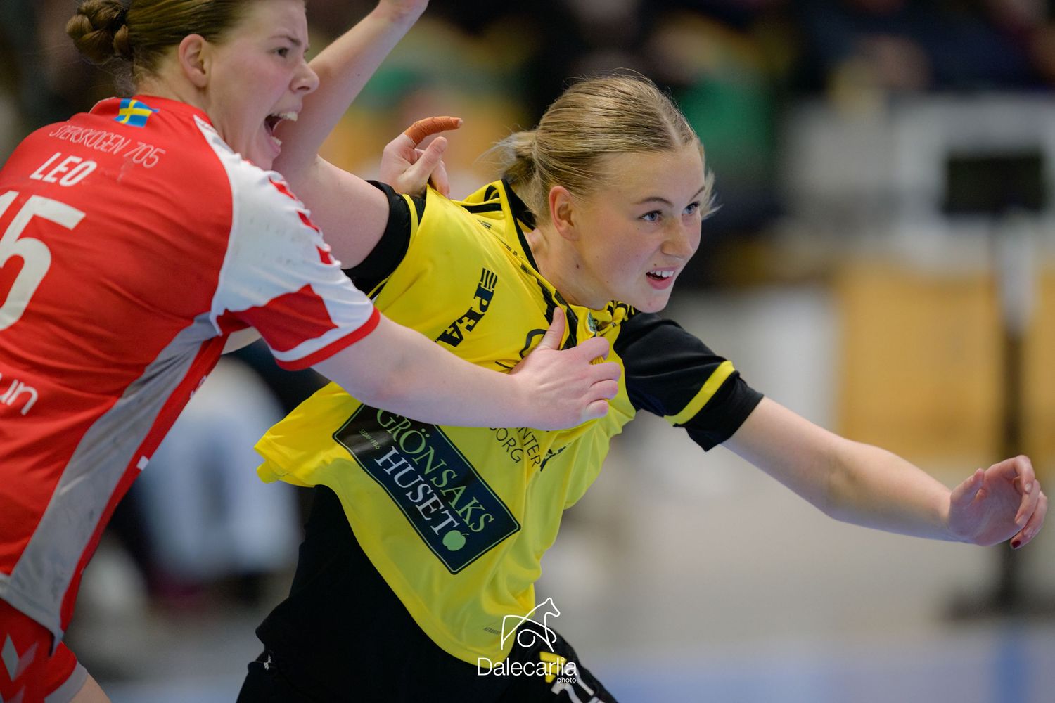 A handball player in a yellow jersey tries to get past a defender in red during an intense match.