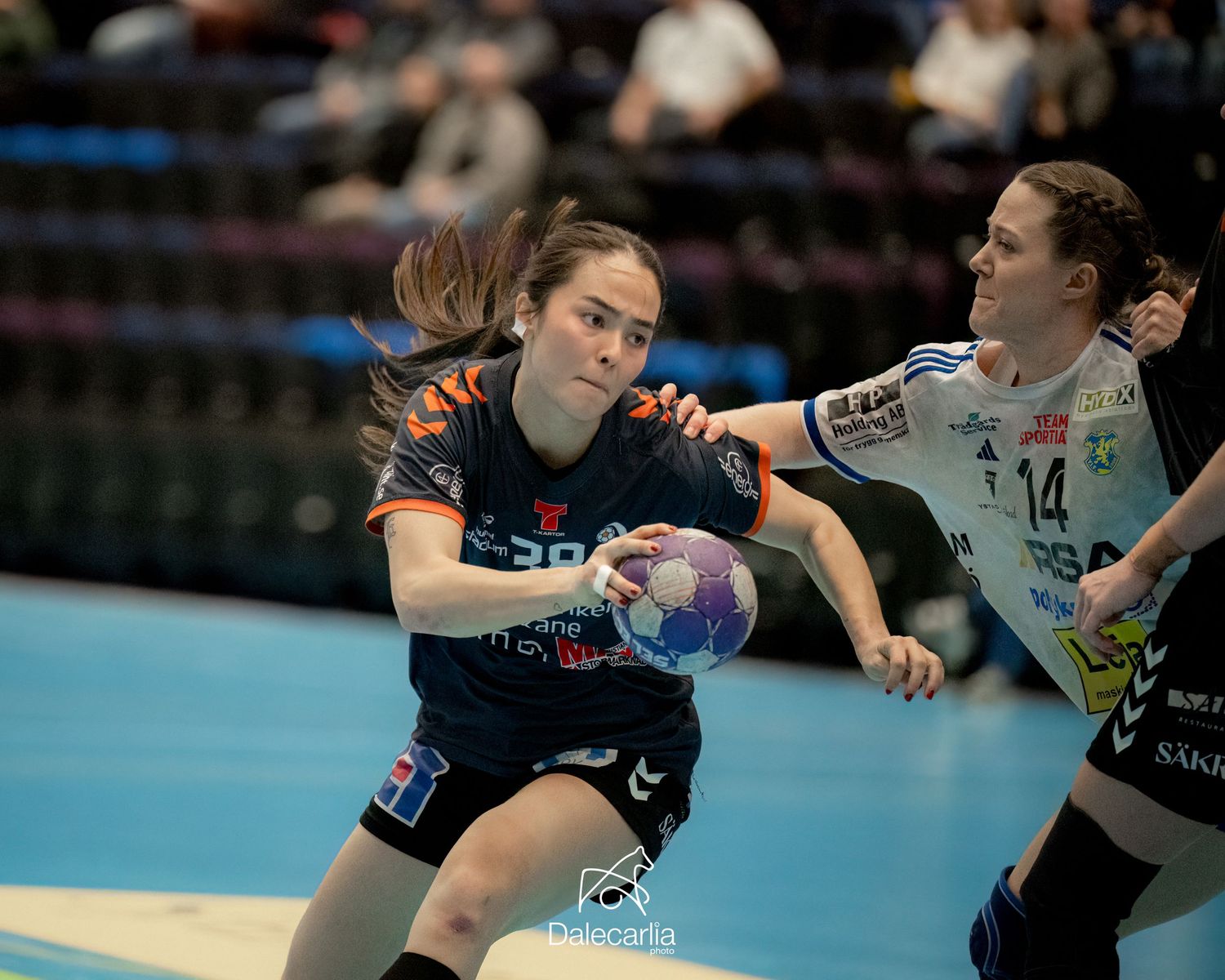 Two handball players compete for the ball during an intense indoor match with one player making a defensive play.