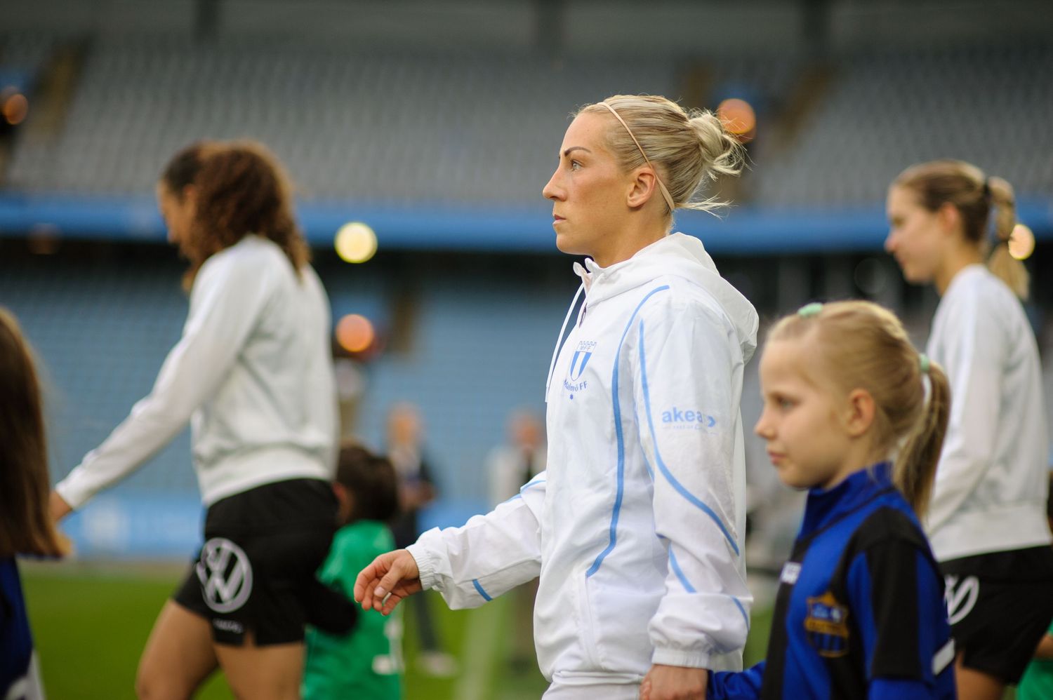 Soccer players on field wearing white and blue uniforms during practice session at stadium.