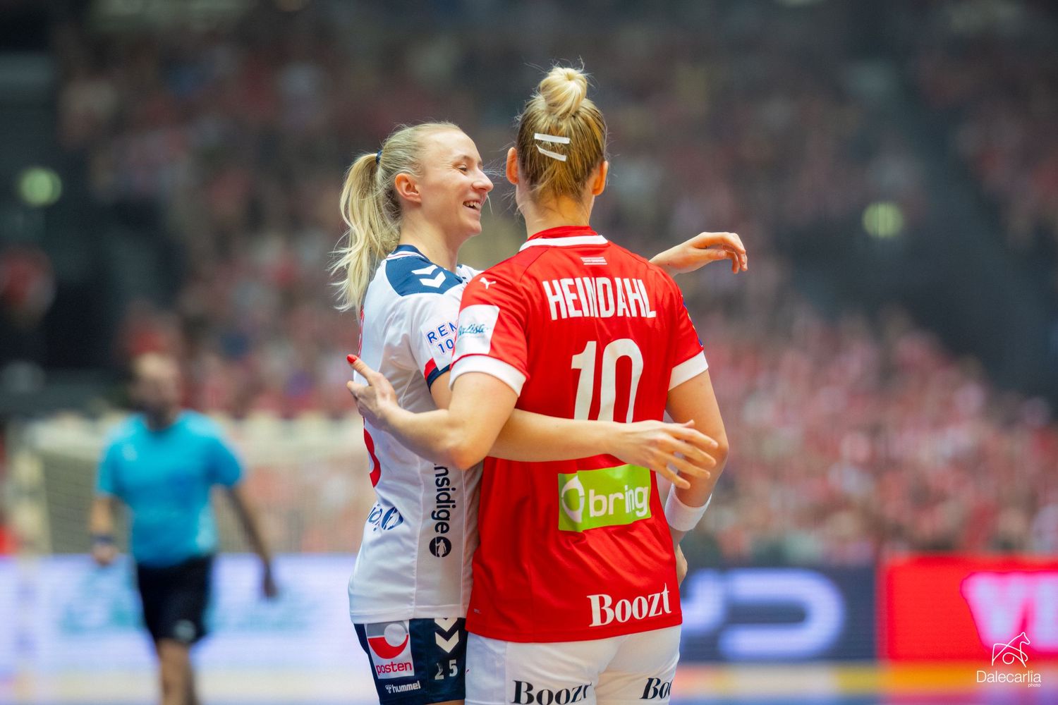 Two handball players embrace on the court during an intense match, with one wearing a red jersey numbered 10.