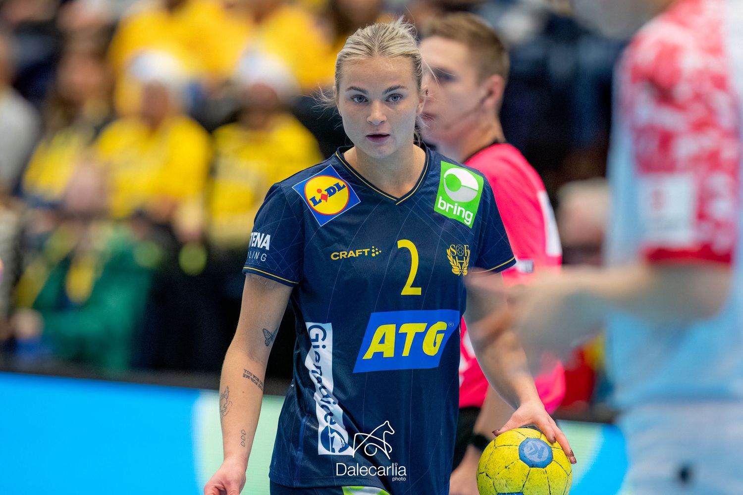 A handball player in a navy blue jersey with number 2 and ATC logo stands ready during a match.