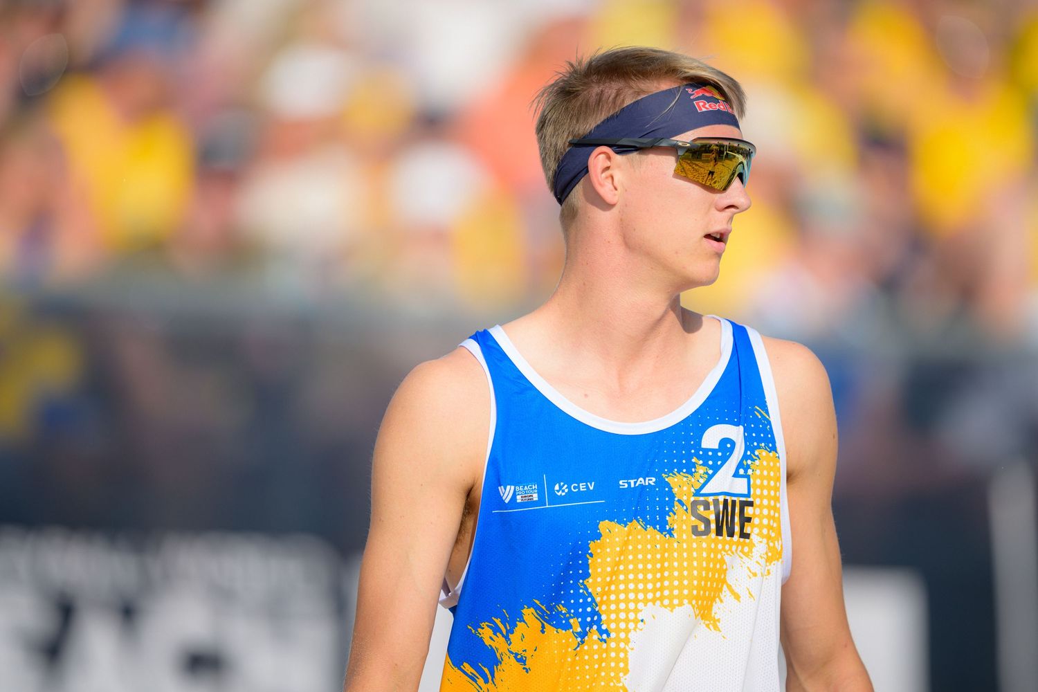 Athlete in blue and yellow jersey and sunglasses stands focused during outdoor competition in bright sunlight.