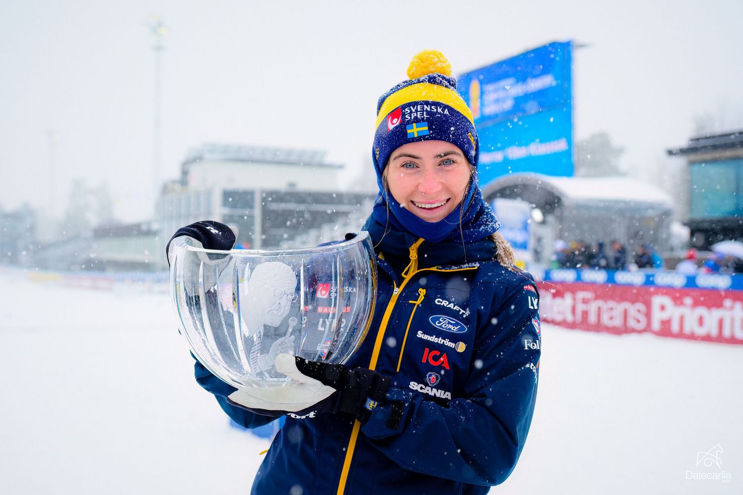 Trophy winner poses in winter sports gear during snowy conditions at sporting event.