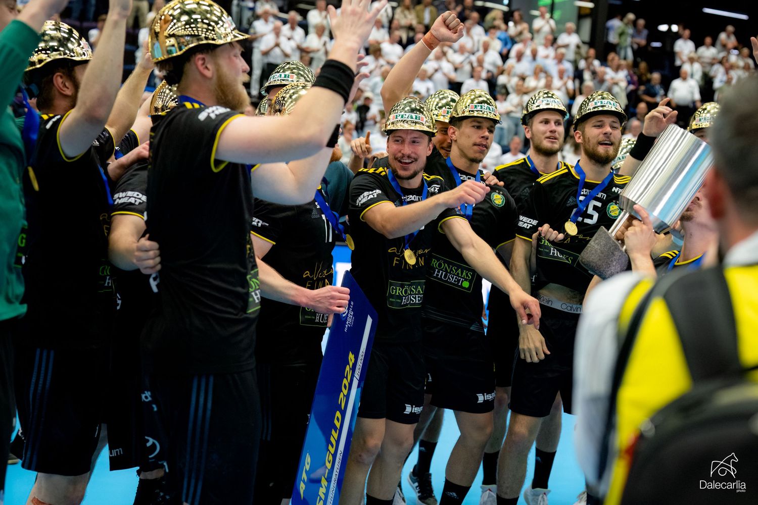 Sports fans in matching black uniforms and leopard print hats cheer enthusiastically during a game.