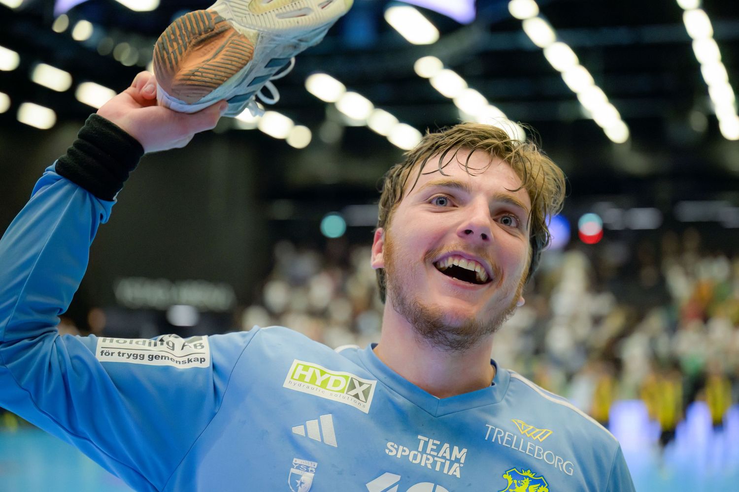 Athlete in light blue jersey celebrates victory by raising trophy during indoor sporting event.