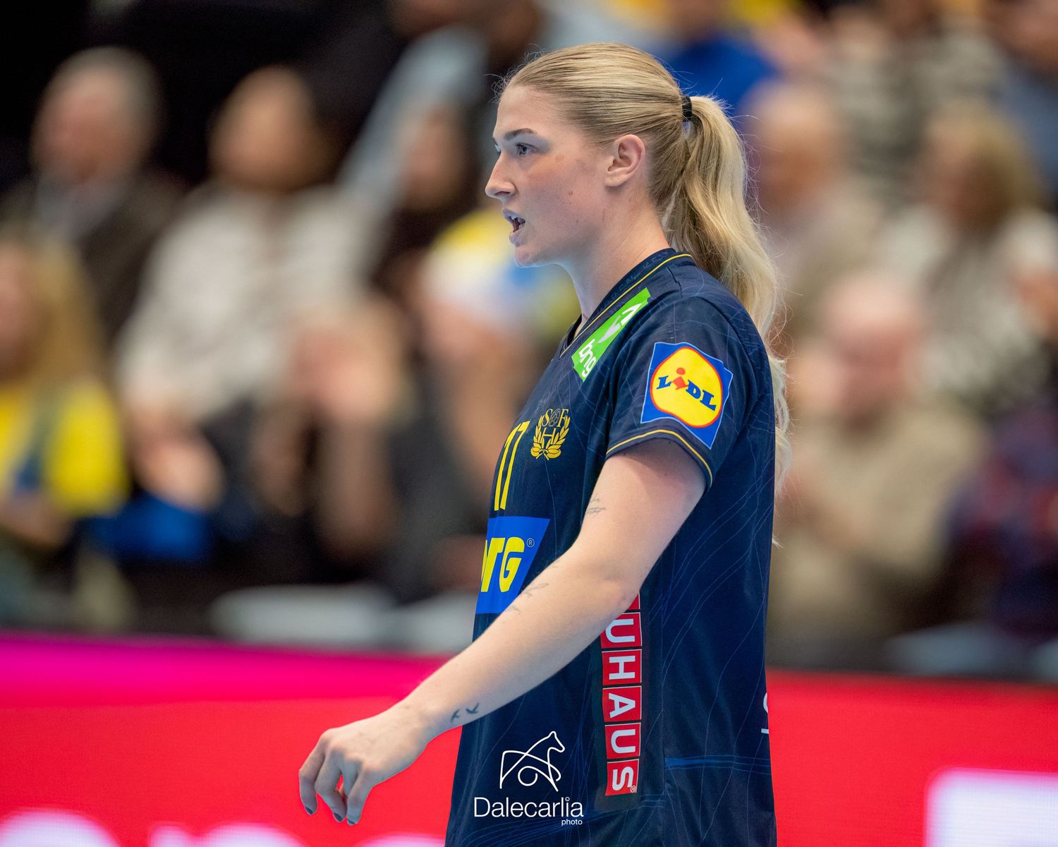 Female handball player in a blue jersey with yellow accents shown during a competitive match.