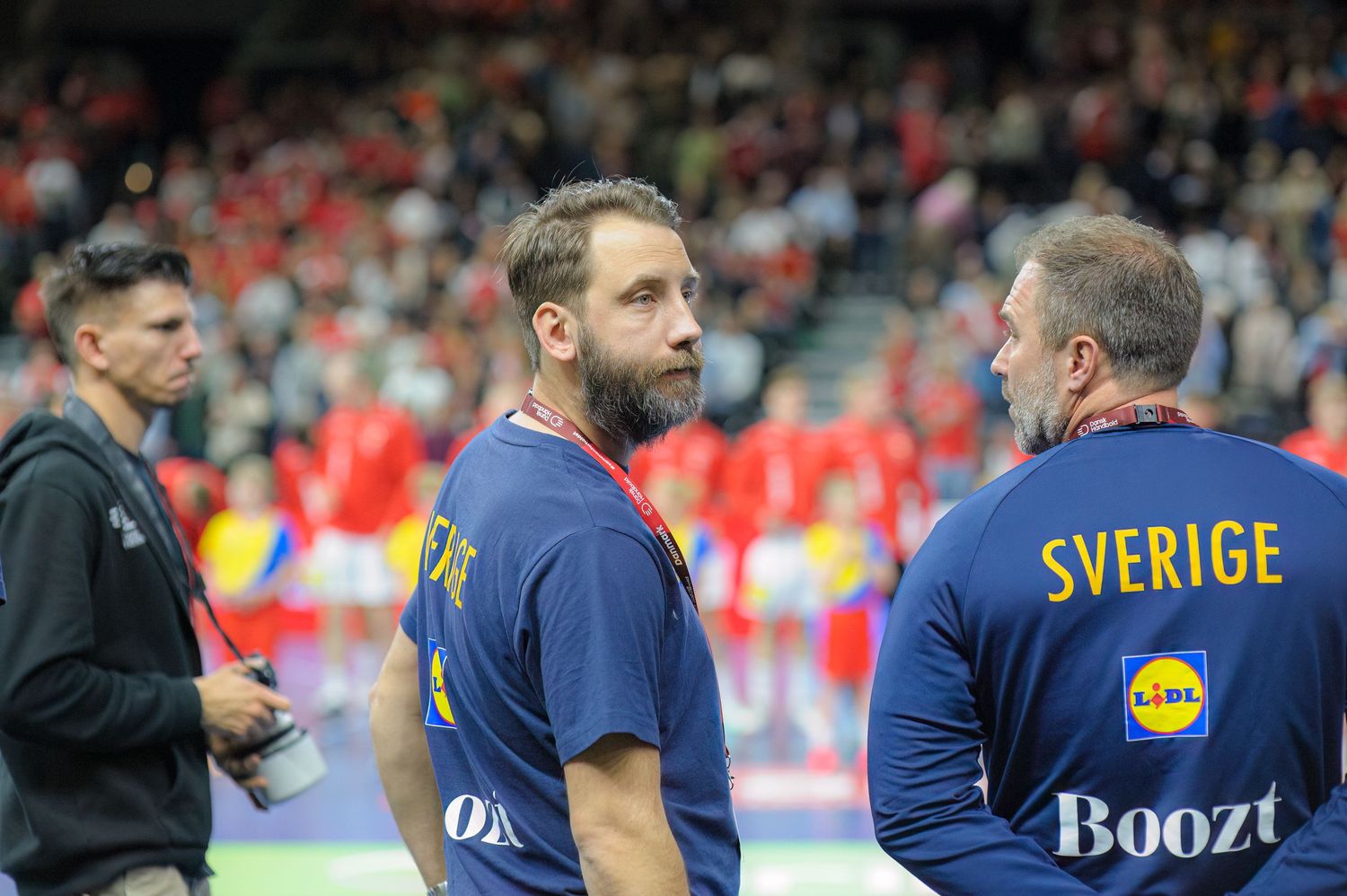 Two sports team members in blue uniforms with Sverige branding stand on a field during a sports event.