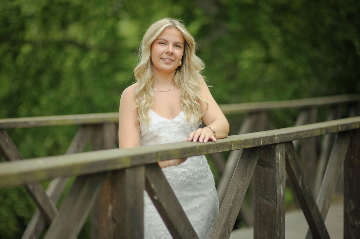 A person in a white lace wedding dress poses on a rustic wooden bridge surrounded by lush greenery.